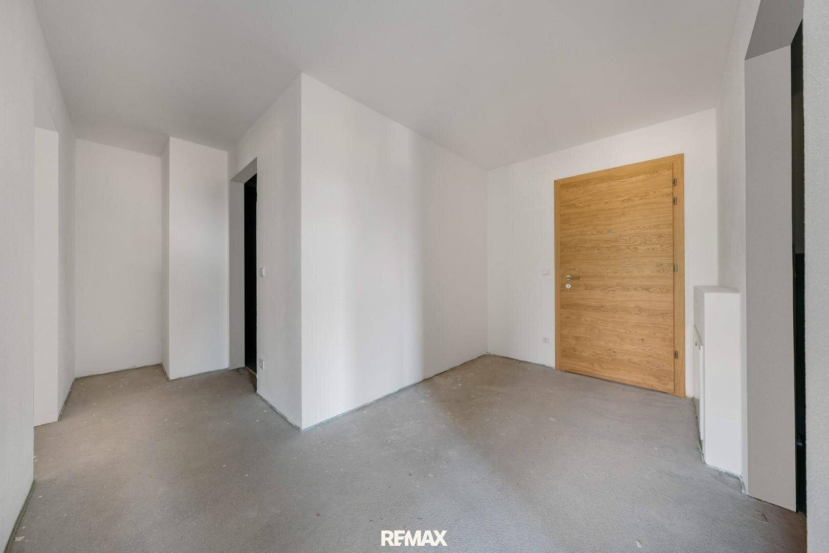 Leerer Raum mit Betonboden und einer modernen Holztür, bereit für die Gestaltung.