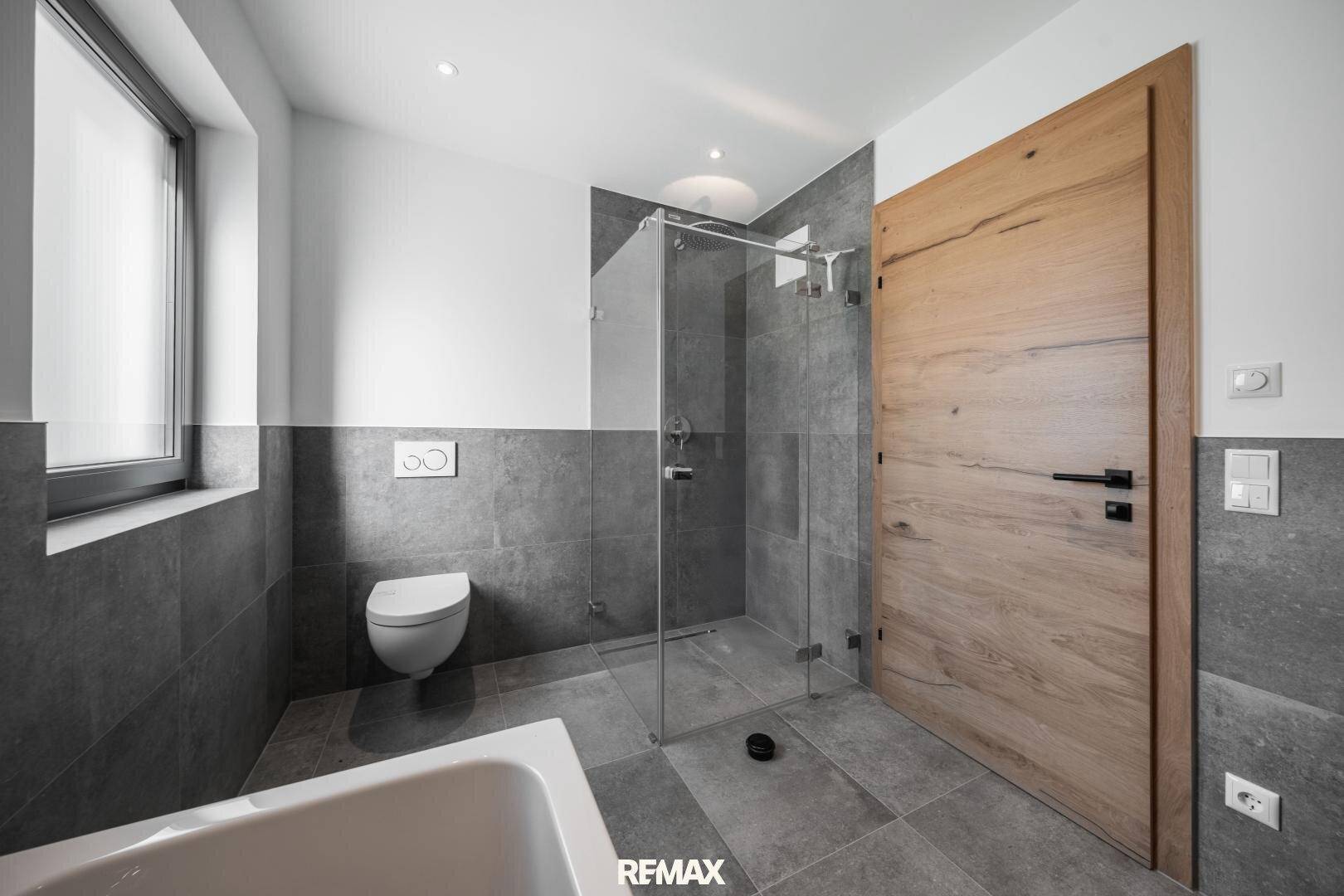 Modernes Badezimmer mit bodengleicher Dusche, wandhängendem WC und Fenster für natürliches Licht.