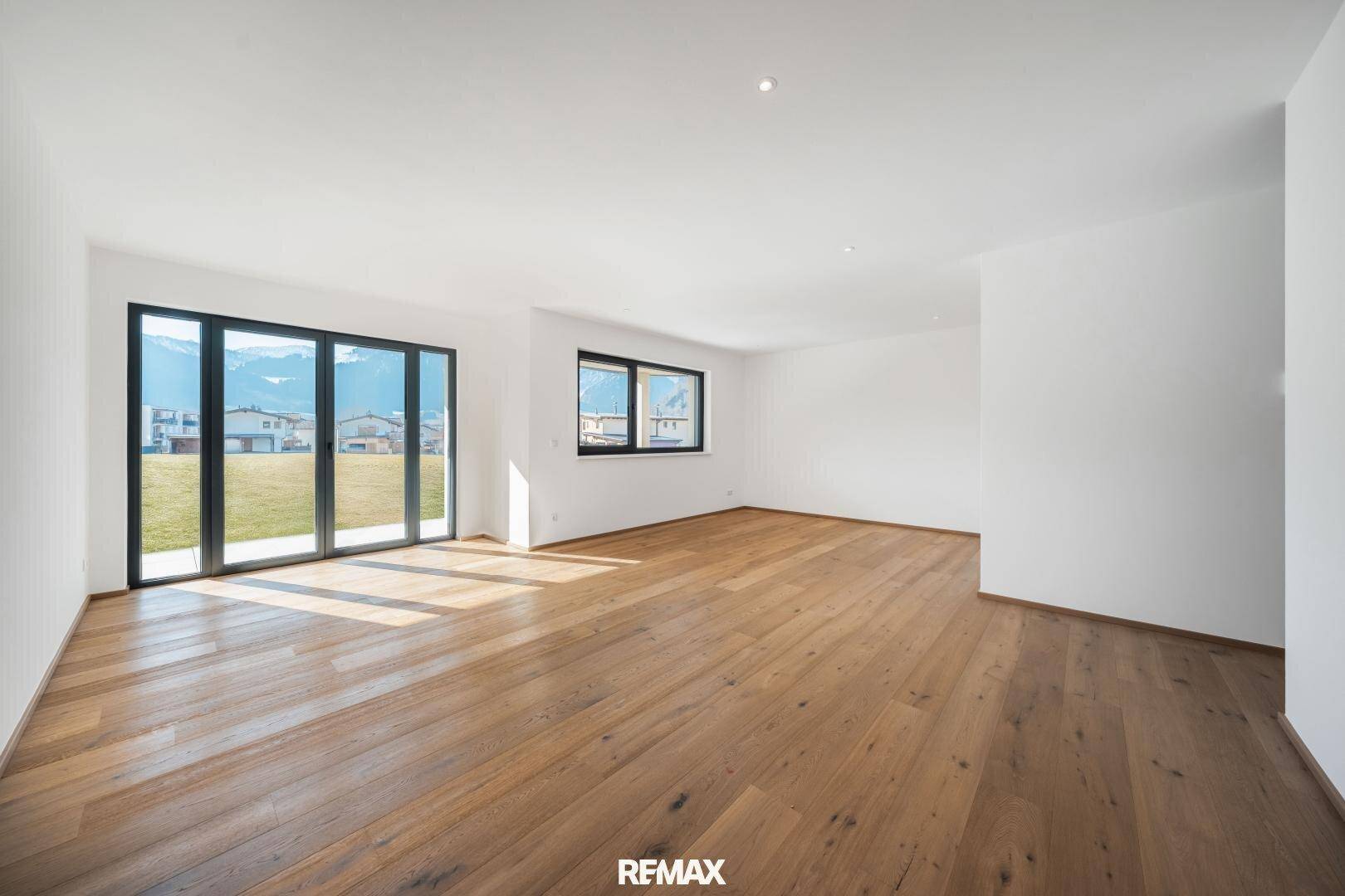 Heller, leerer Raum mit Holzboden und großen Fenstern, die einen weiten Blick auf die Berge bieten.