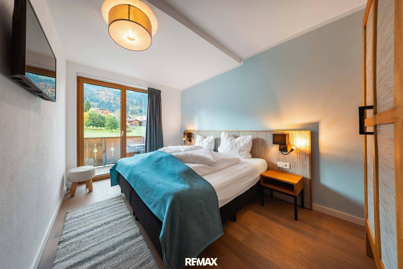 Gemütliches Schlafzimmer mit Balkonzugang, Holzboden und Blick auf die Berge.