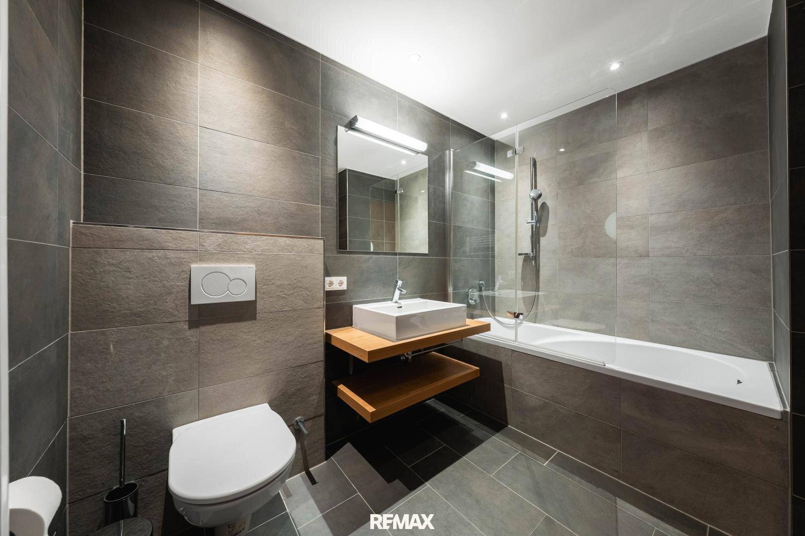 Modernes Badezimmer mit Badewanne, wandhängendem WC und dunklen Fliesen.