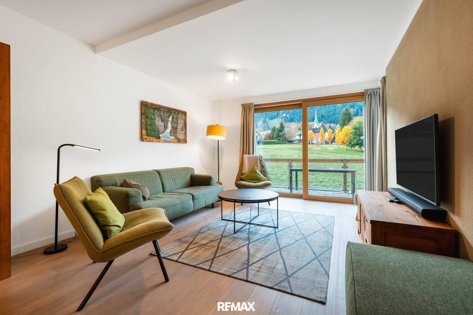 Helles Wohnzimmer mit modernen Möbeln, Holzboden und großem Fenster mit weitem Blick ins Grüne.