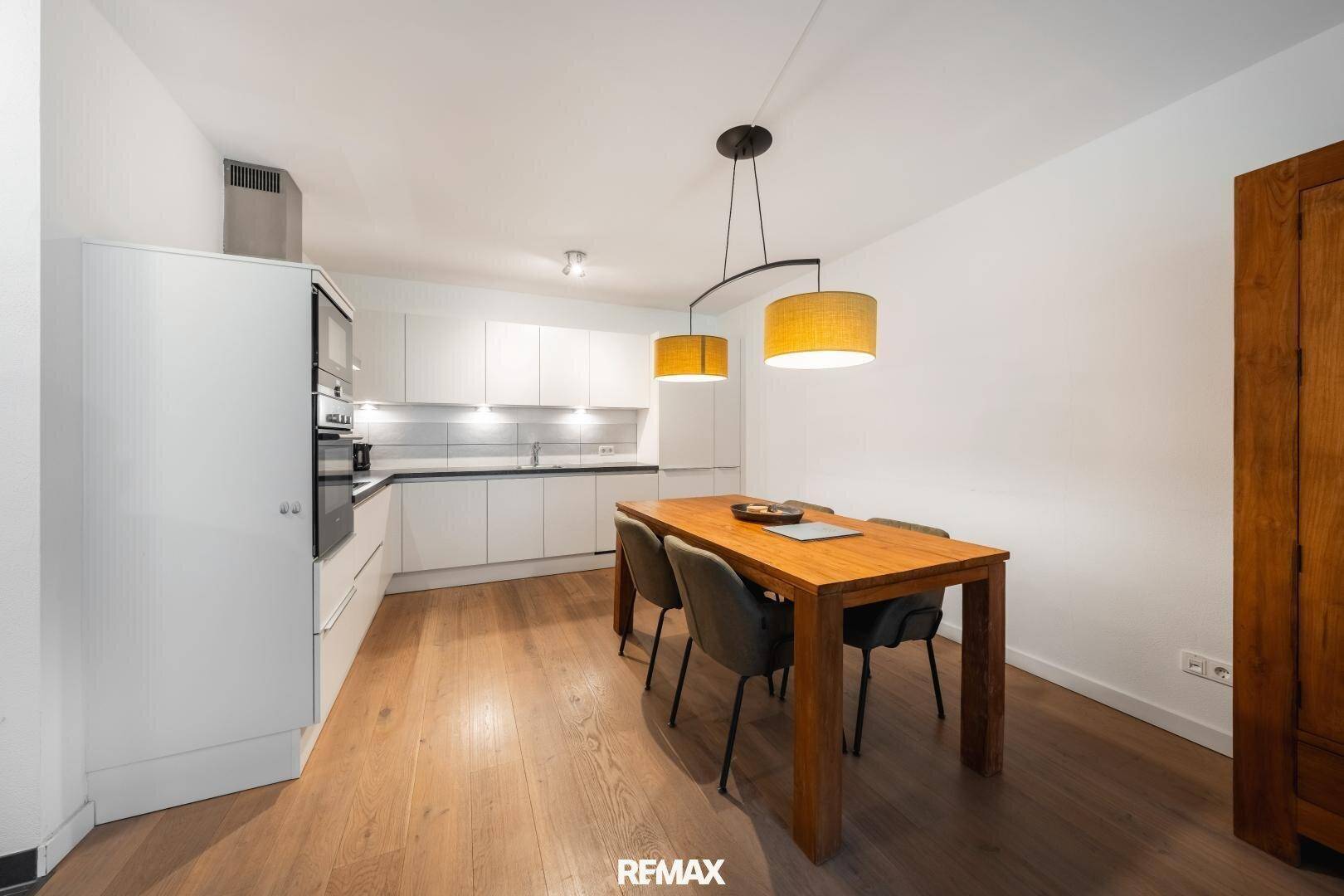 Helle, moderne Wohnküche mit weißer Einbauküche, Esstisch und Holzboden.