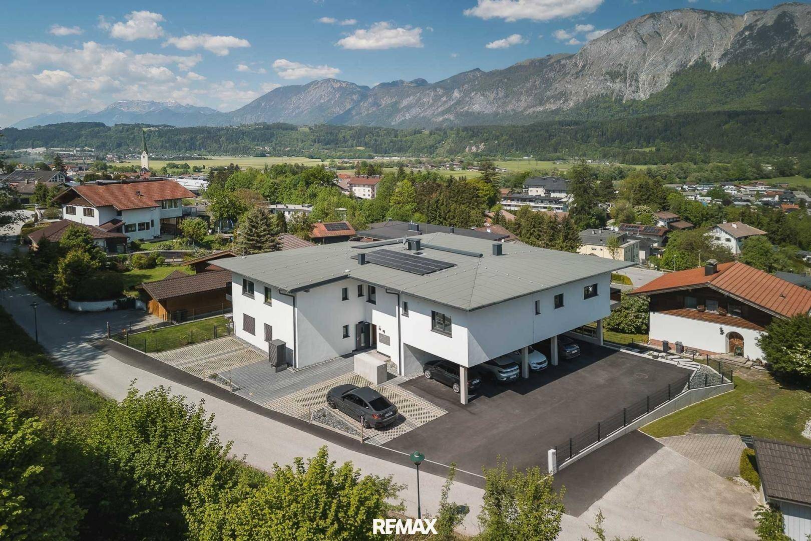 Neubau mit moderner Architektur, Photovoltaikanlage und Tiefgaragenstellplätzen in alpiner Landschaft.