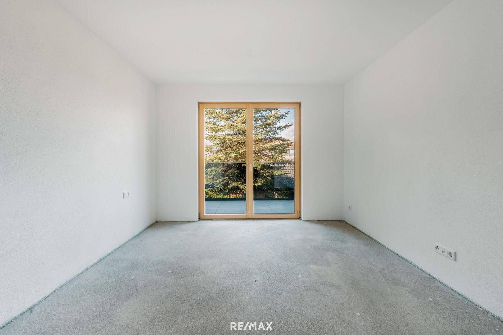 Leerer Raum mit Betonboden und großer Glasschiebetür, die viel Tageslicht hereinlässt.