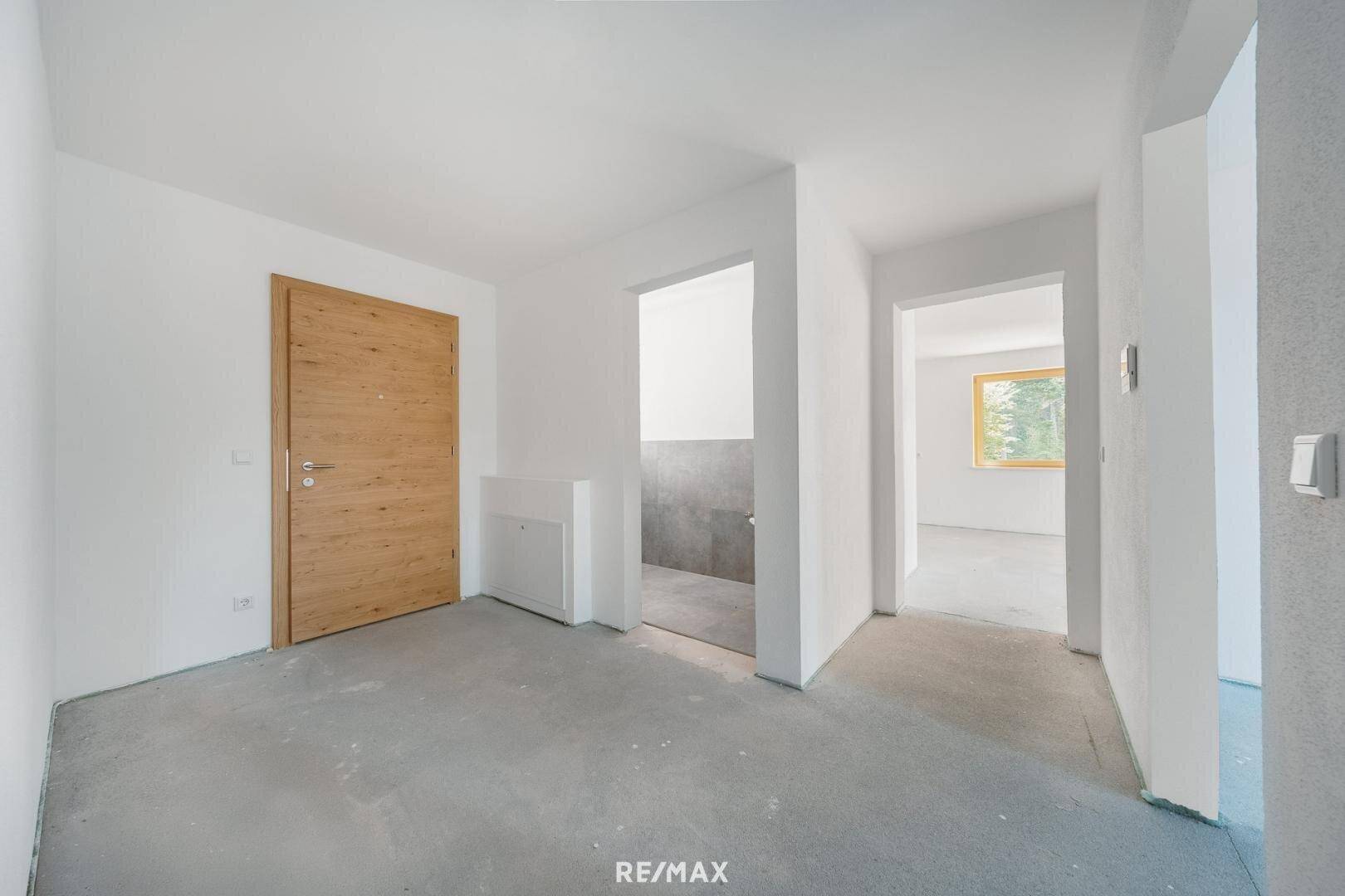 Heller Flur mit Betonboden, Holztür und Zugängen zu weiteren Räumen der Wohnung.