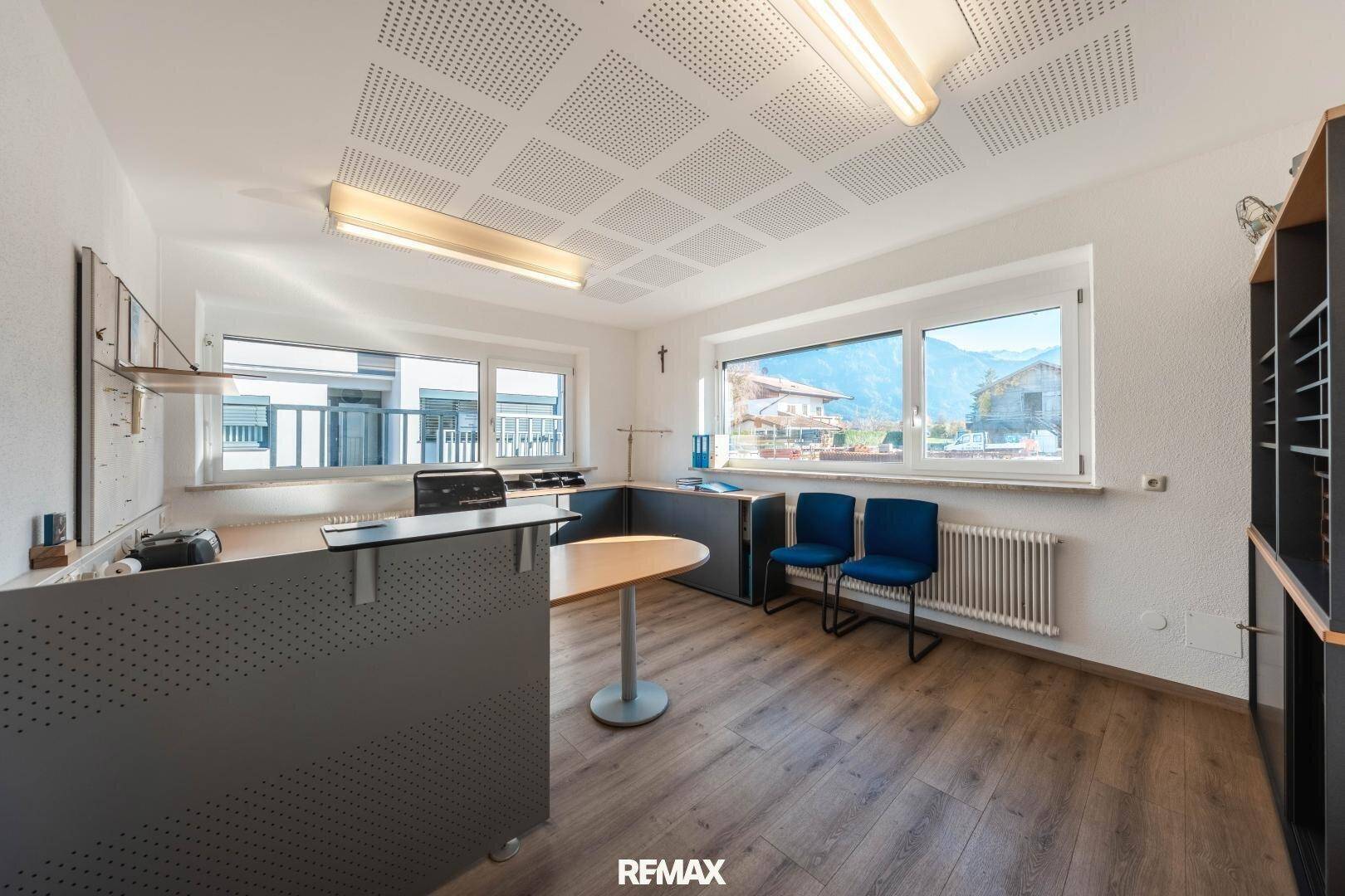 Helles Büro mit großen Fenstern, Holzboden, funktionaler Einrichtung und Blick auf die Berge.