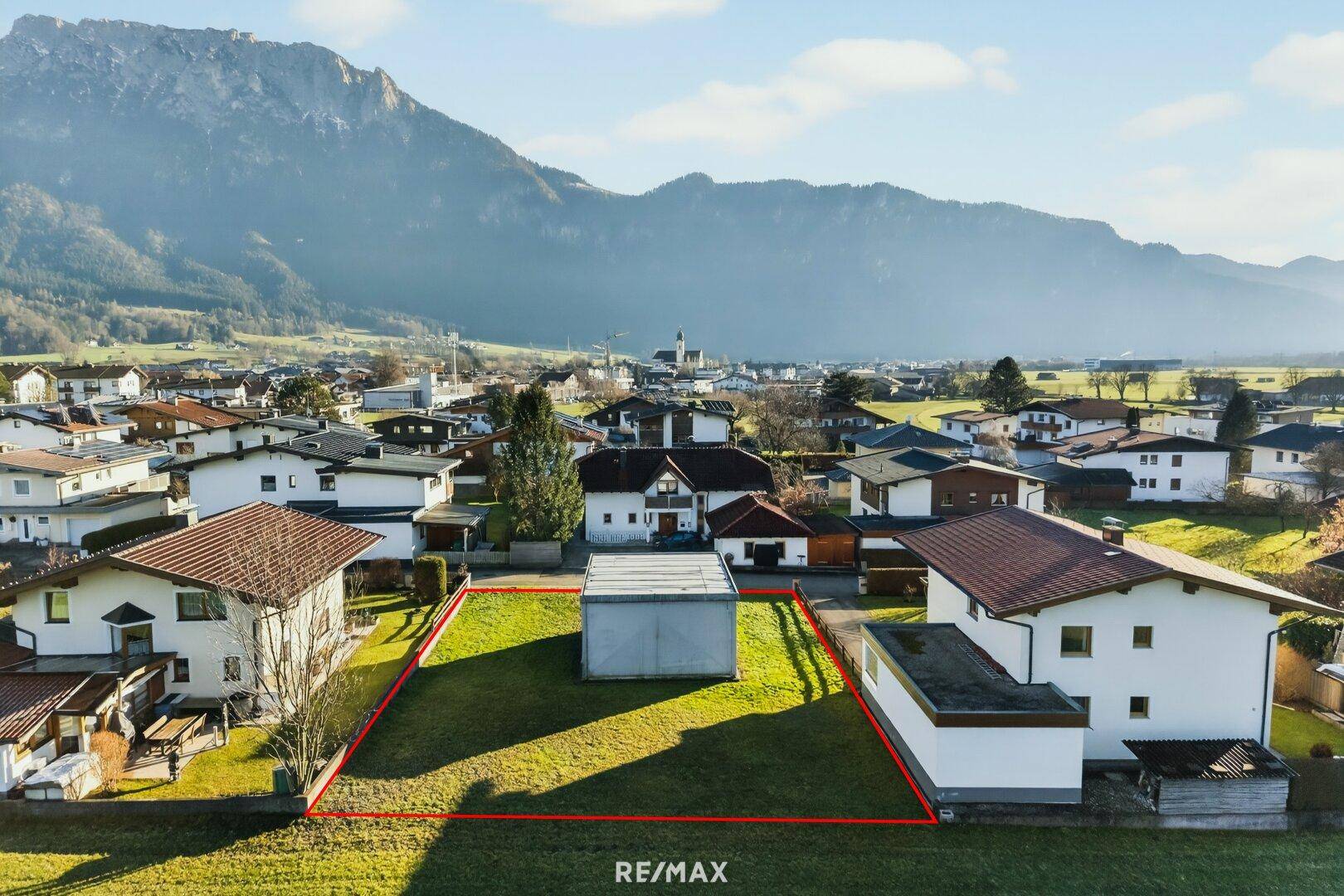 Nahaufnahme des Baugrundstücks mit roter Umrandung und einem kleinen Gebäude, umgeben von Grünflächen.