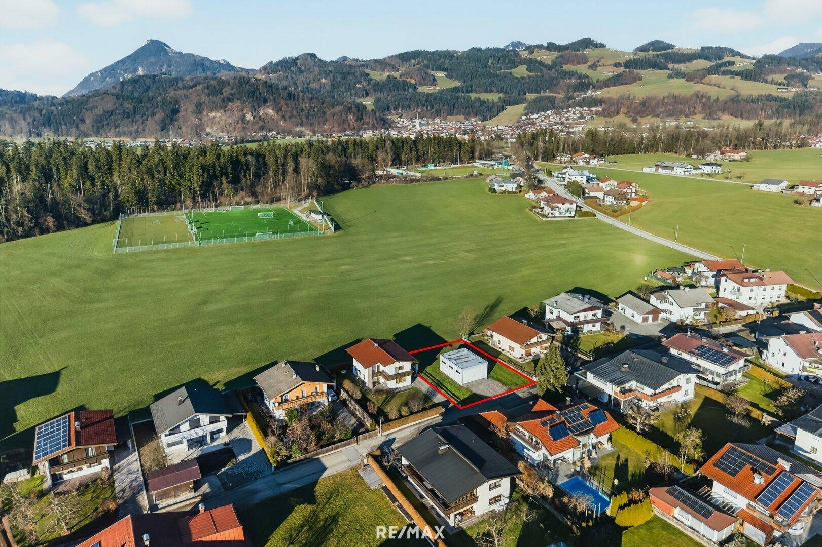 Blick von oben auf ein Baugrundstück in einer Siedlung, angrenzend an grüne Felder und einen Sportplatz.