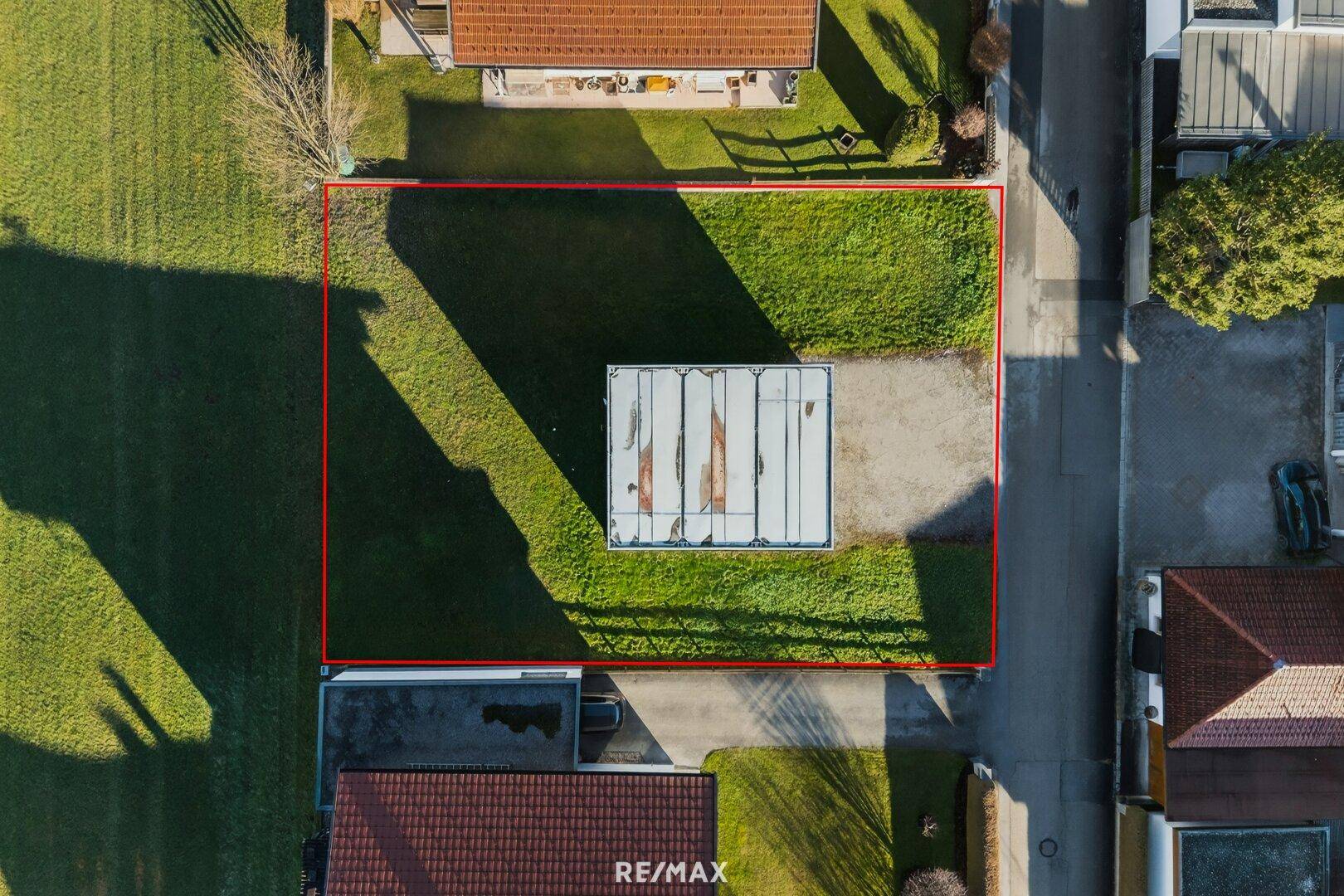 Direkte Draufsicht auf das rechteckige Baugrundstück mit Rasenfläche und angrenzender Straße.