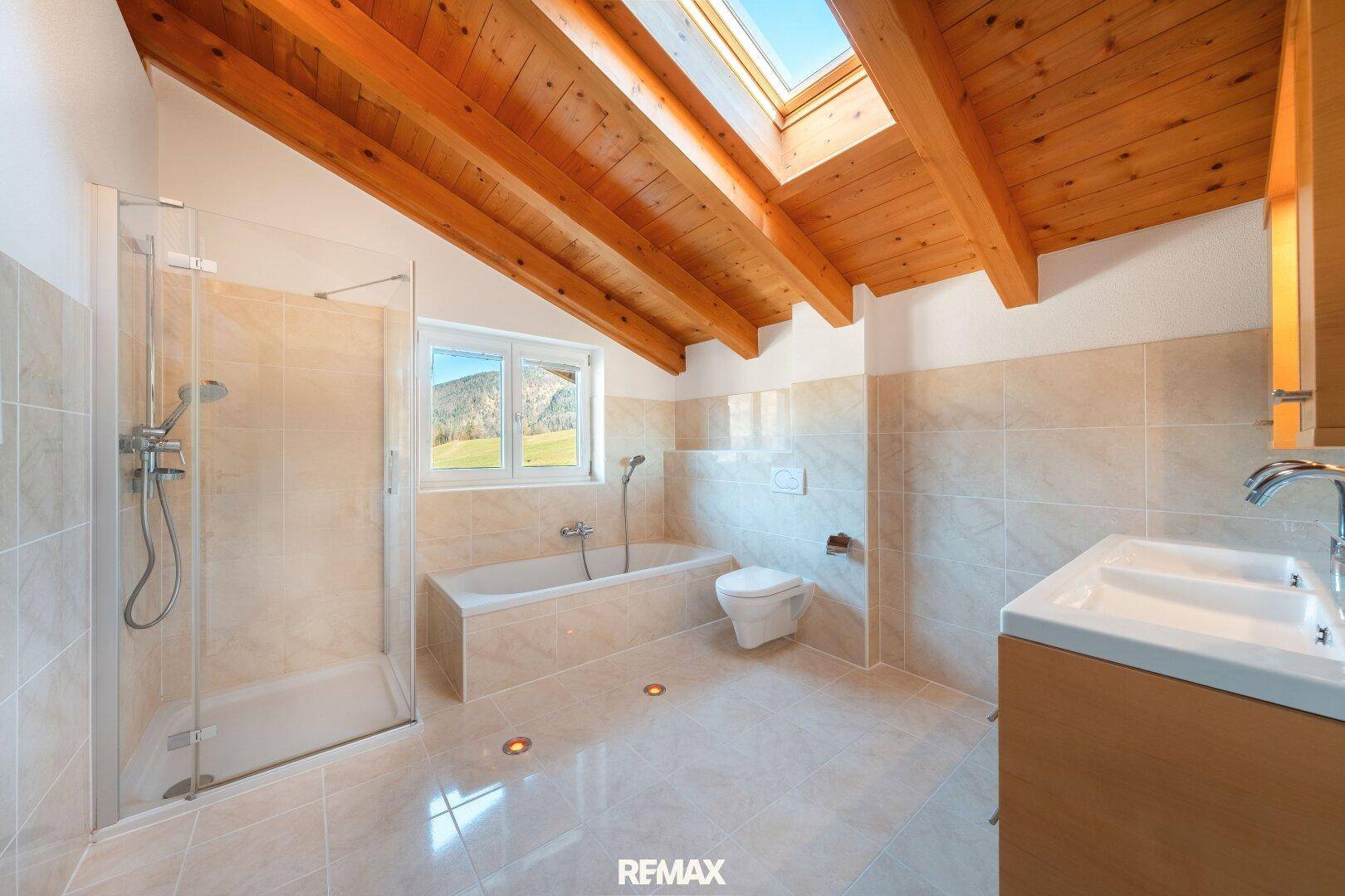 Helles Badezimmer mit Holzbalkendecke, Badewanne, Dusche und Dachfenster.