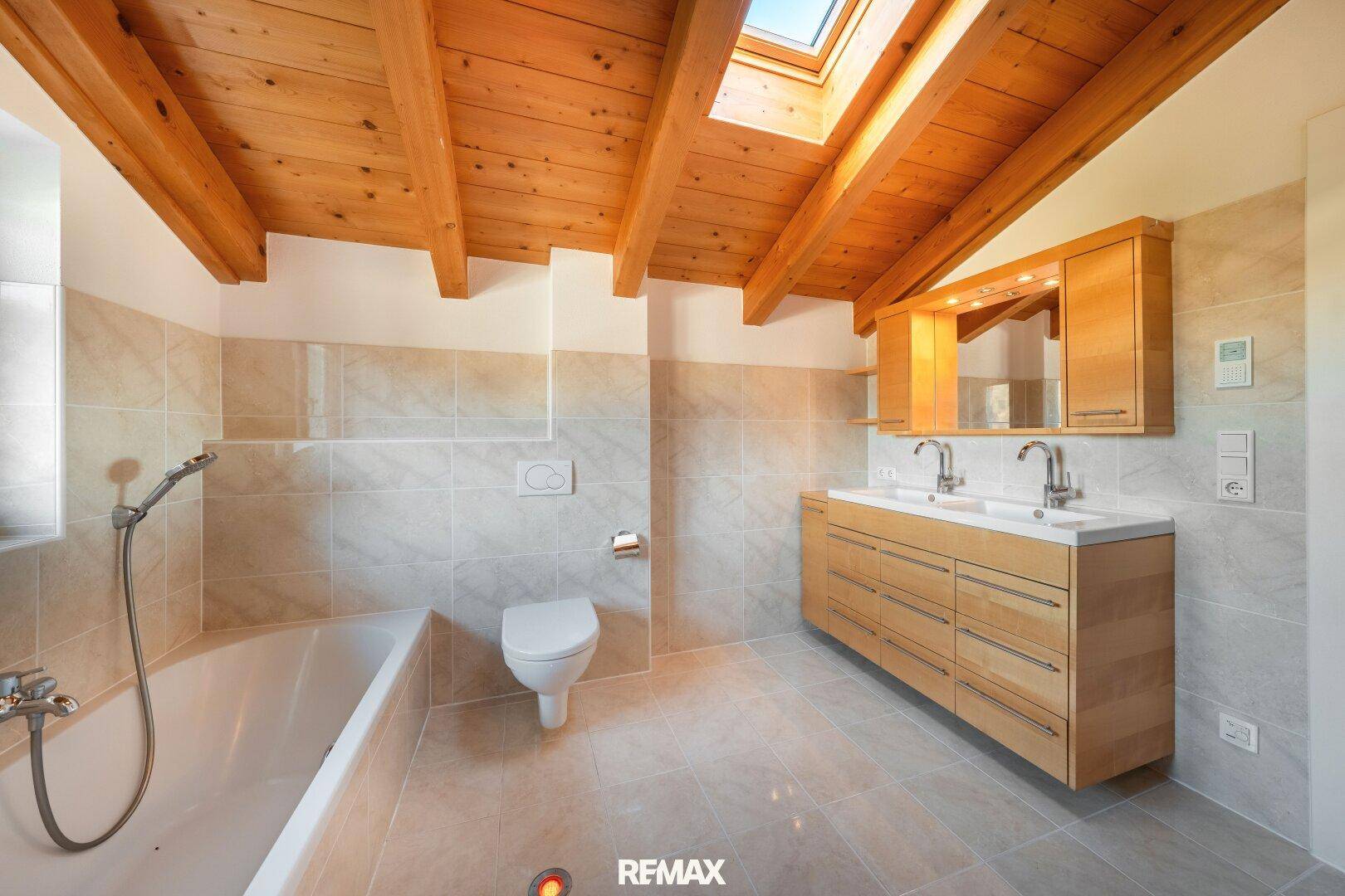 Geräumiges Badezimmer mit Doppelwaschbecken, Badewanne und Holzbalkendecke.