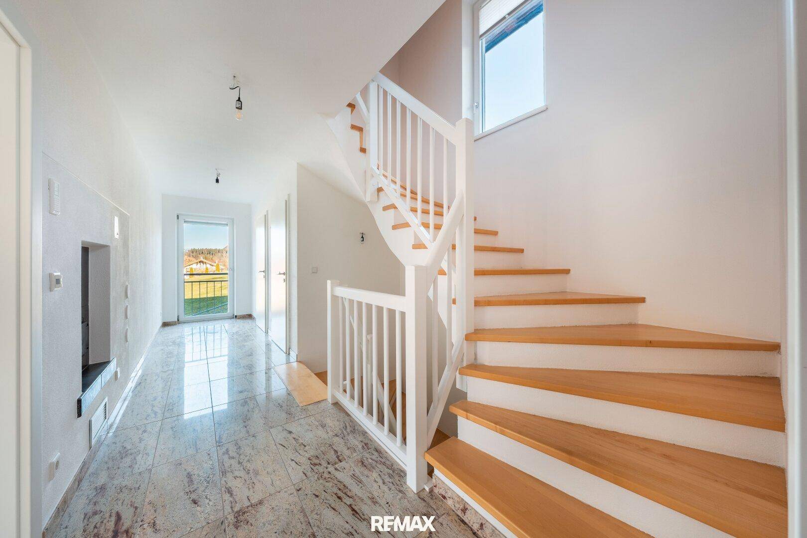 Heller Flur mit Holztreppe, Fliesenboden und Zugang zu weiteren Räumen.