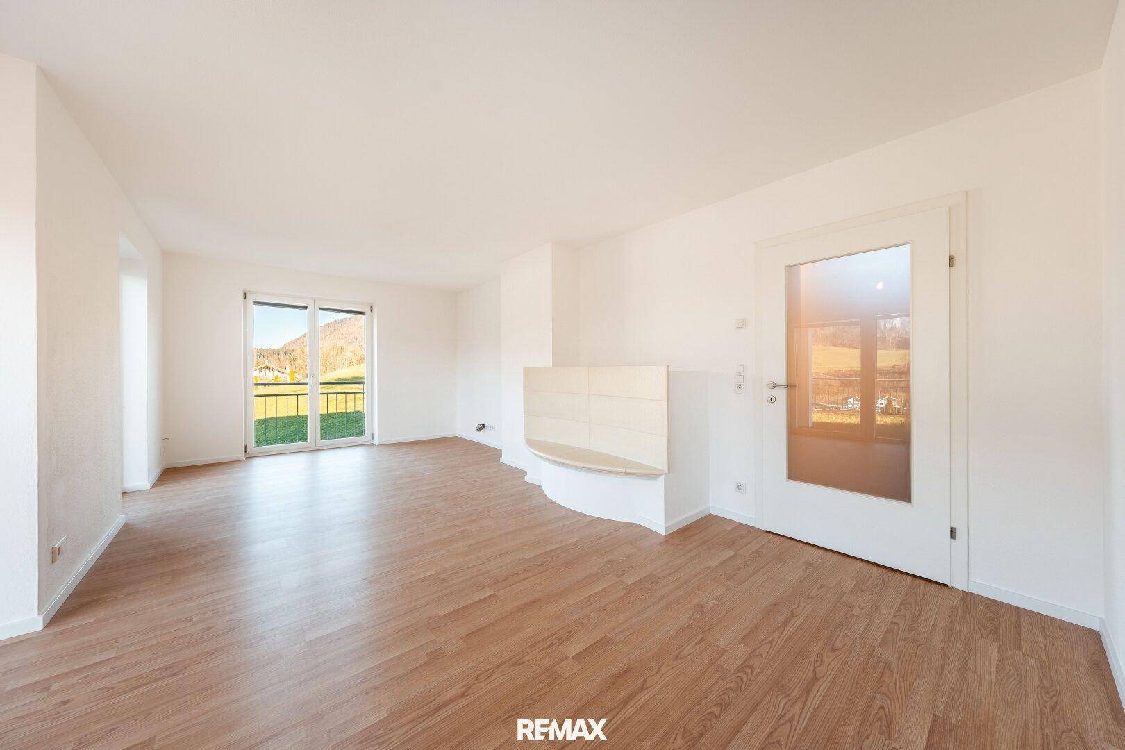 Geräumiges, leeres Wohnzimmer mit Laminatboden und Zugang zu einem Außenbereich.