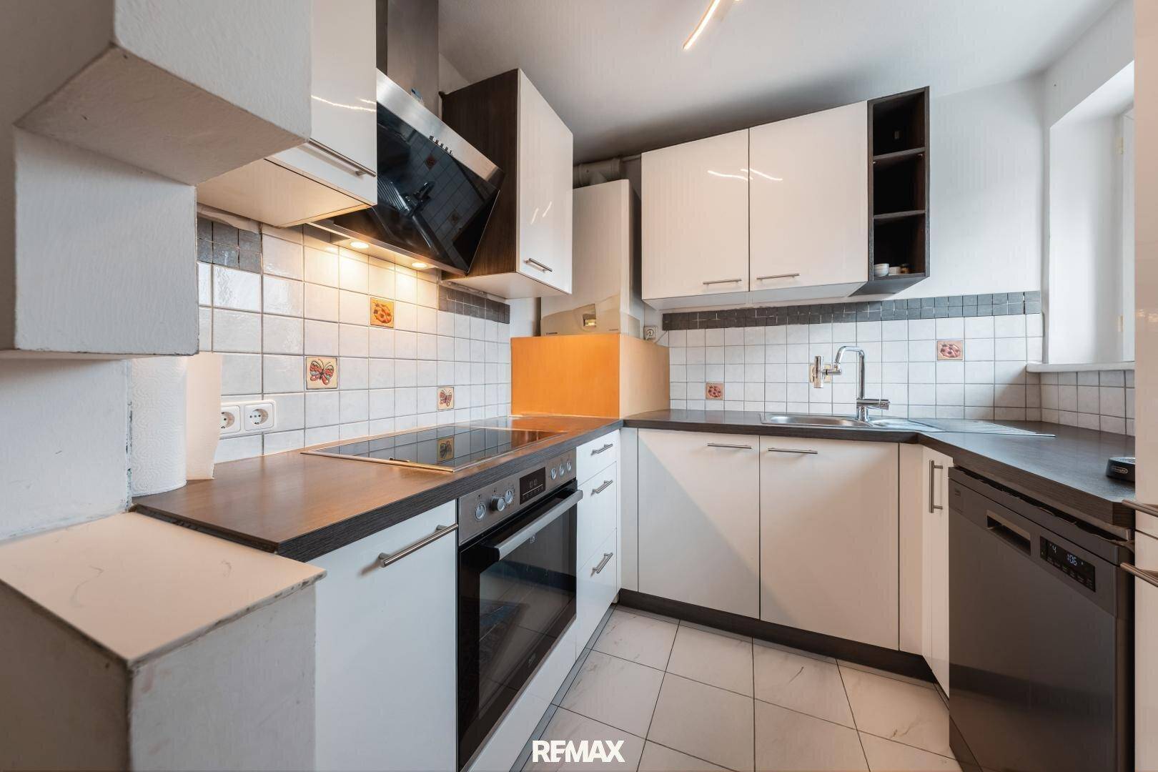 Funktionale Küche mit weißen Schränken, dunklen Arbeitsplatten und gefliestem Spritzschutz, ausgestattet mit modernen Geräten und einem Fenster.