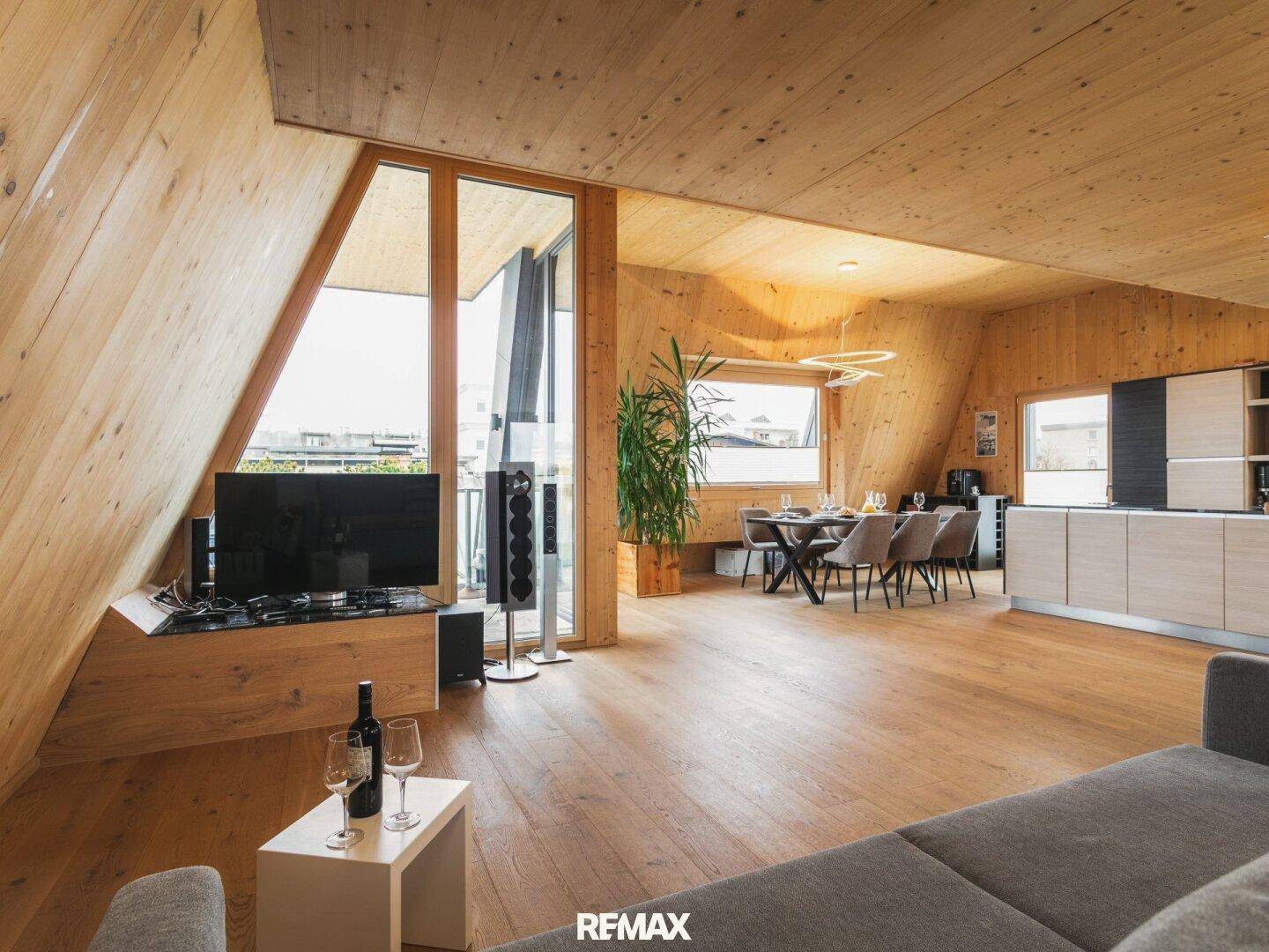 Heller Wohnbereich mit Holzböden, großen Fenstern und Essbereich, integriert in die offene Küche.