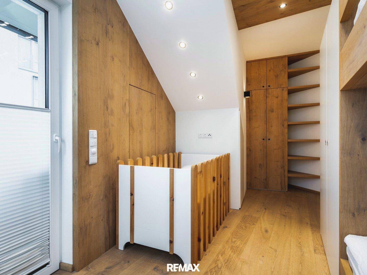 Raum mit Holzwänden, Einbauschränken und einem Babybett unter einer Dachschräge.