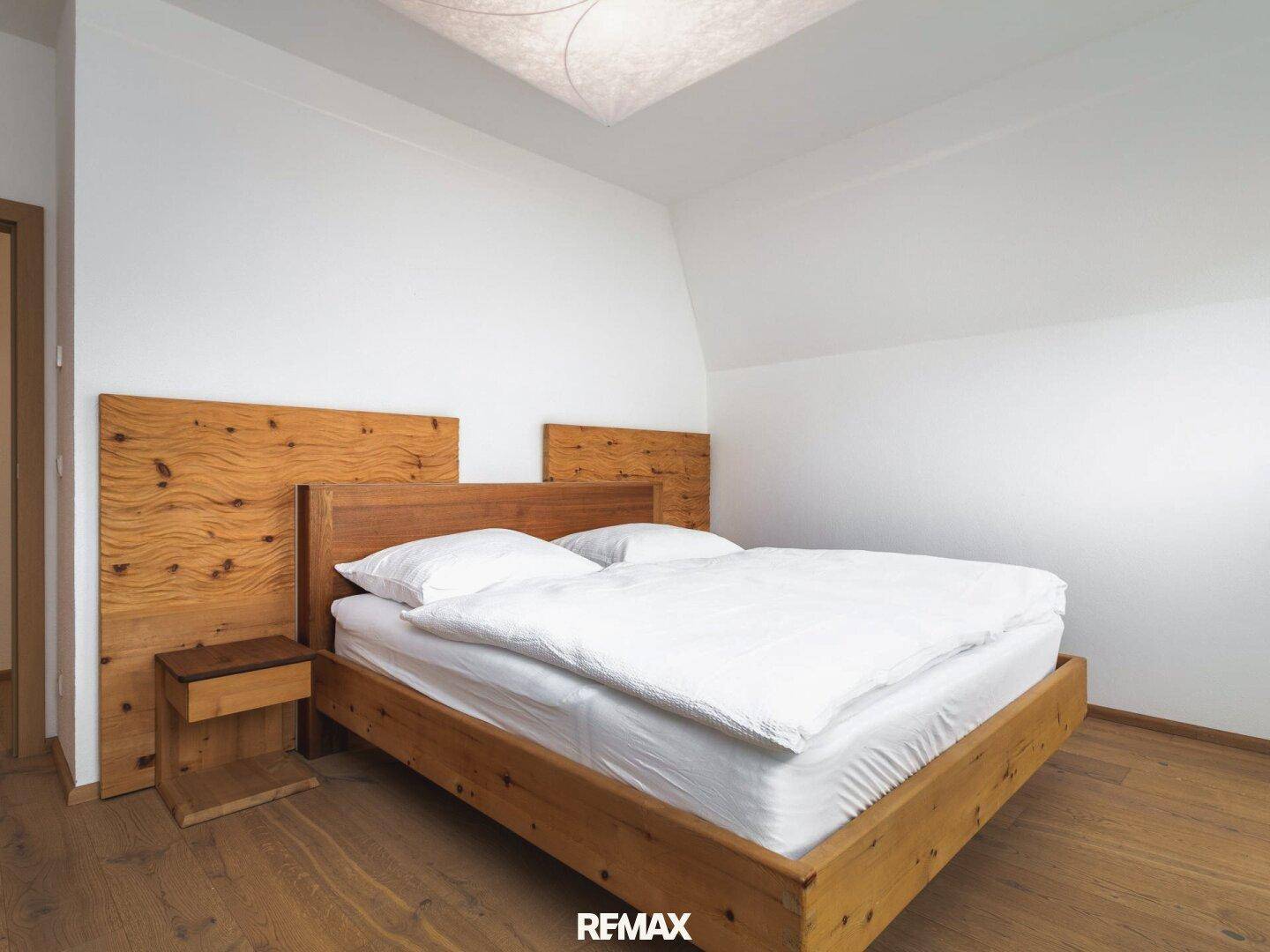 Gemütliches Schlafzimmer mit Holzbett, Holzboden und weiß gestrichenen Wänden unter einer Dachschräge.