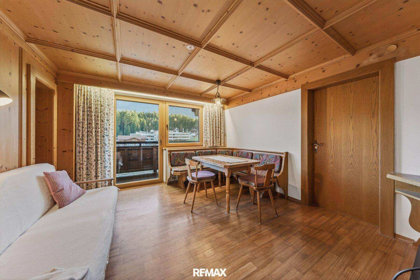 Wohnbereich im alpinen Stil mit Holztäfelung, Essbereich und Balkonzugang.