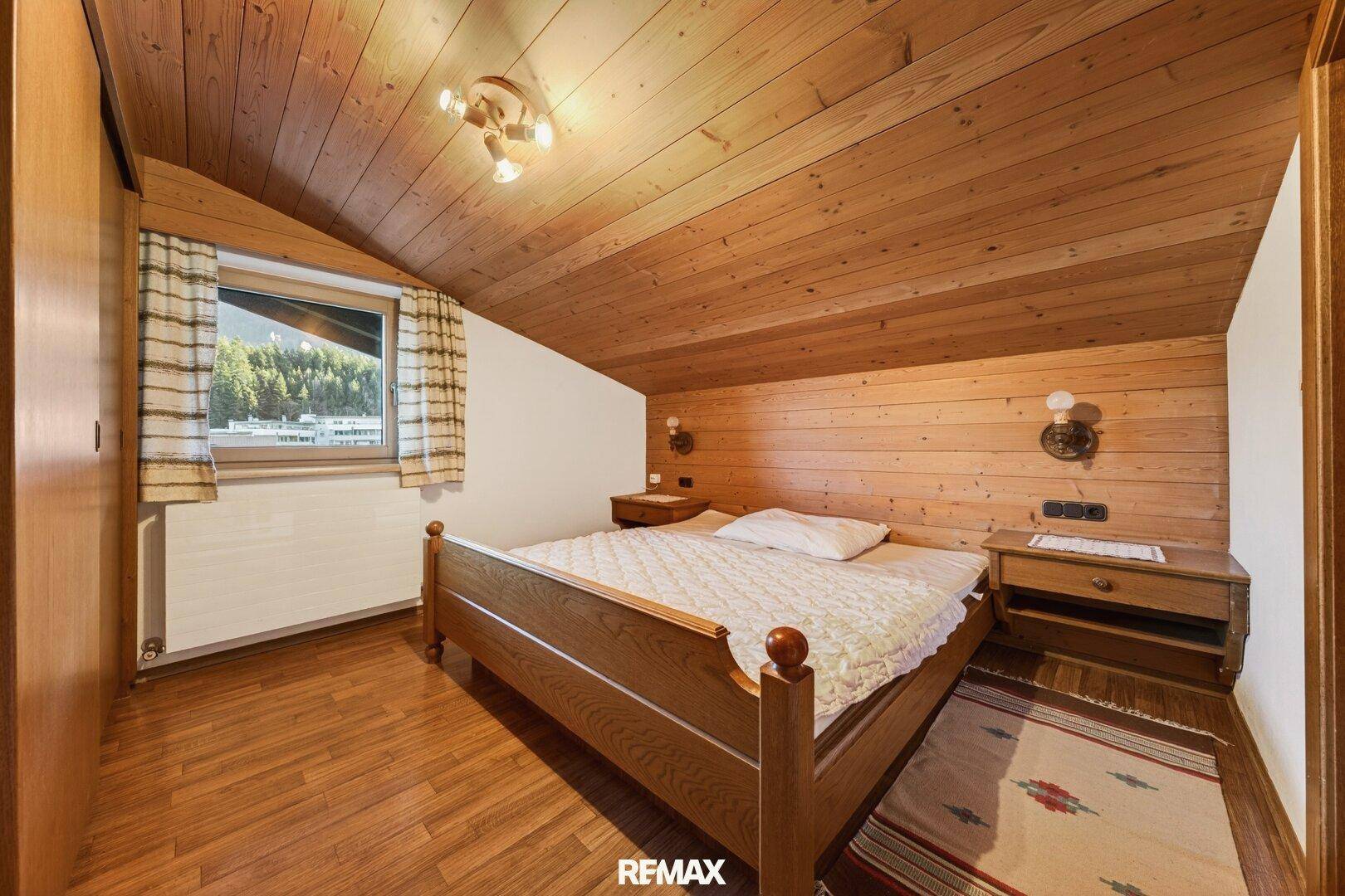 Gemütliches Schlafzimmer im Dachgeschoss mit Holztäfelung, Holzboden und schrägen Decken.