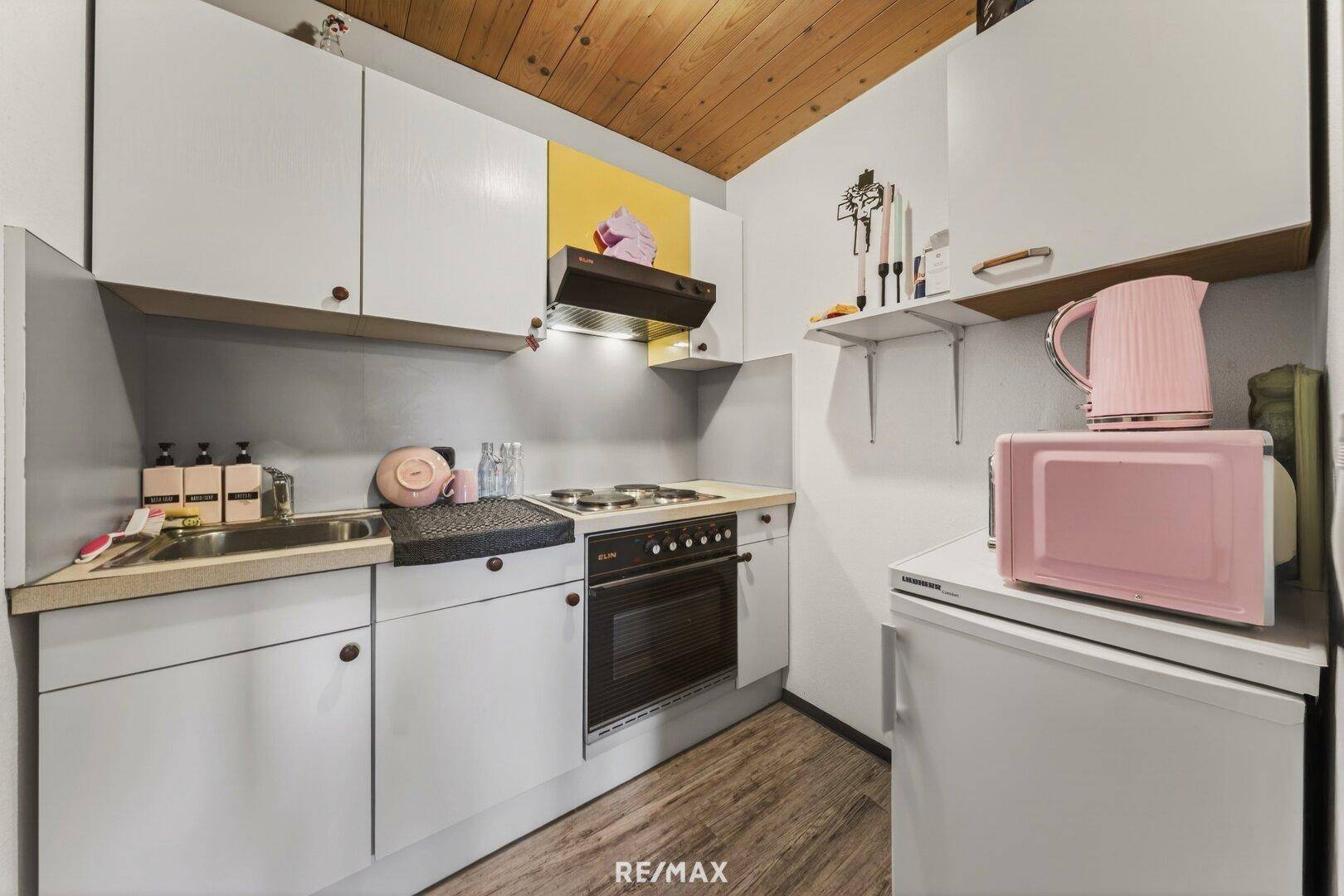 Kleine Küchenzeile mit weißen Schränken, Elektroherd und pinkfarbenen Akzenten.