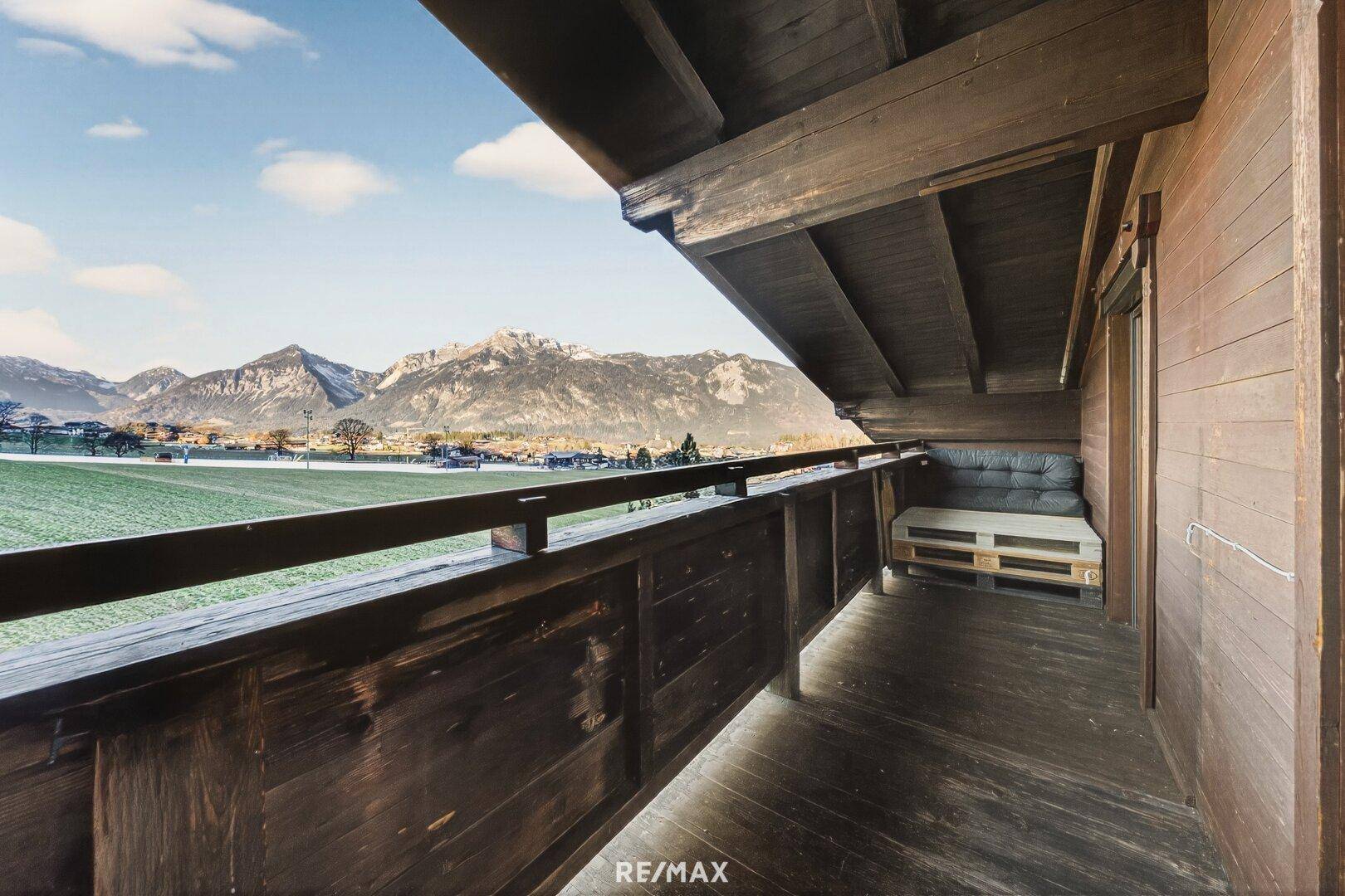 Geräumiger Holzbalkon mit Sitzgelegenheiten und weitem Blick auf die Berge und Landschaft.
