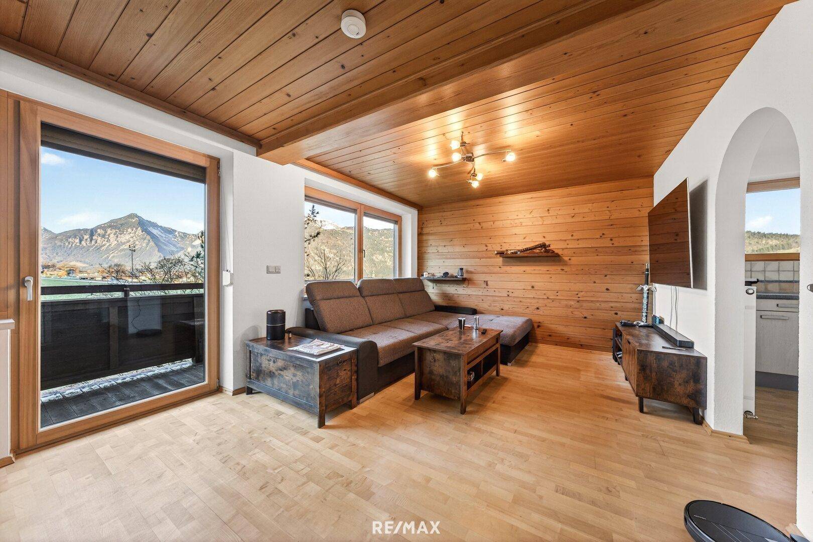 Wohnzimmer mit Holzwänden, Holzboden und Zugang zu einem Balkon mit Bergblick.