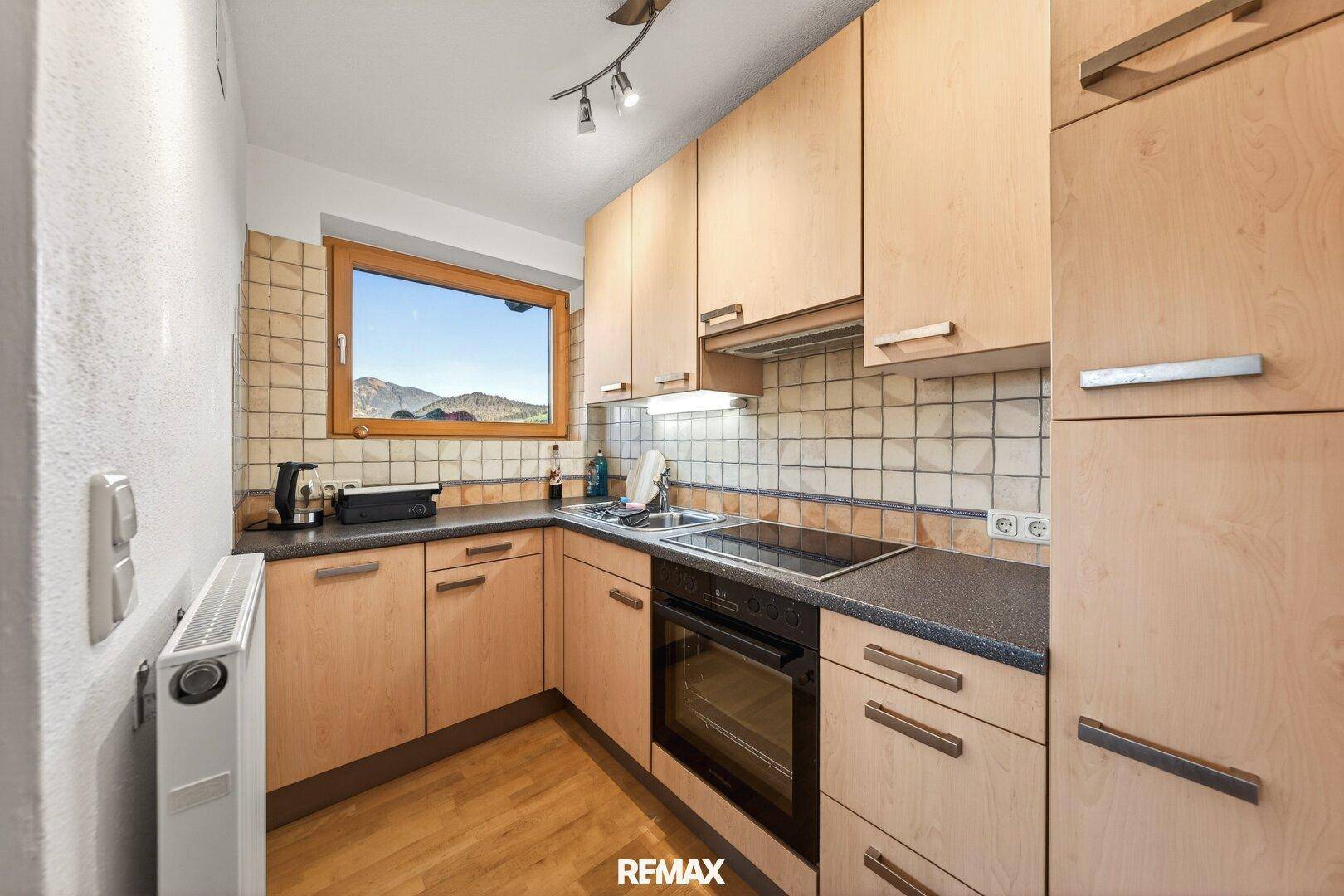 Kleine, funktionale Küche mit Holzschränken, Fliesenrückwand und Fenster mit Bergblick.