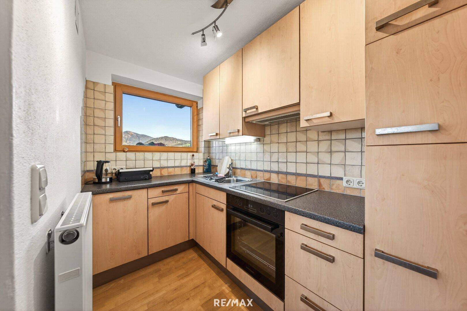 Funktionale Küche mit Holzschränken, Fliesenrückwand und Fenster mit Bergblick.