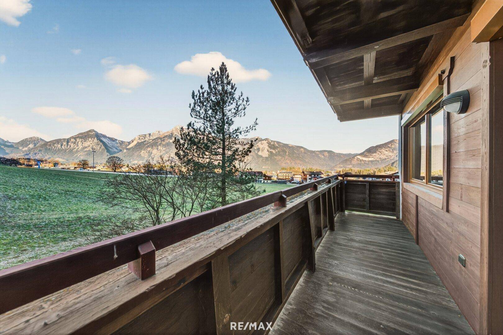 Langer Holzbalkon mit Blick auf die grüne Landschaft und die umliegenden Berge.