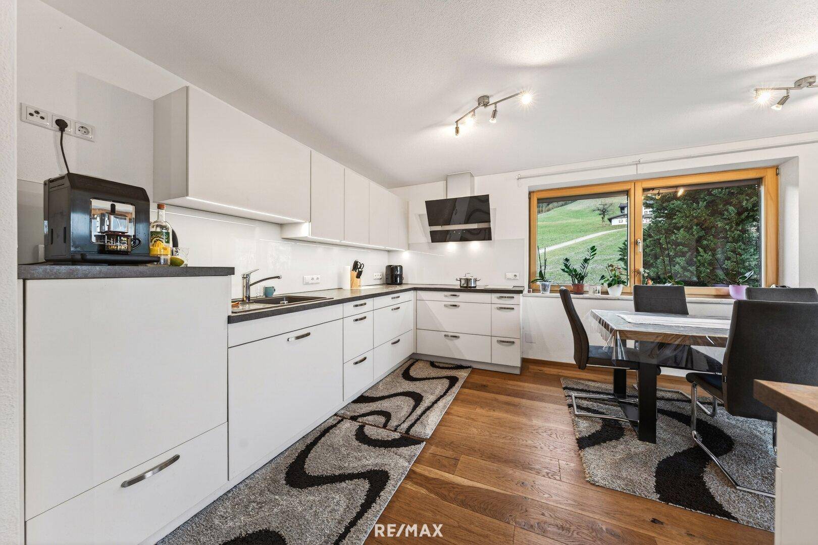 Moderne Küche mit weißen Schränken, Essbereich und Blick auf die grüne Landschaft.