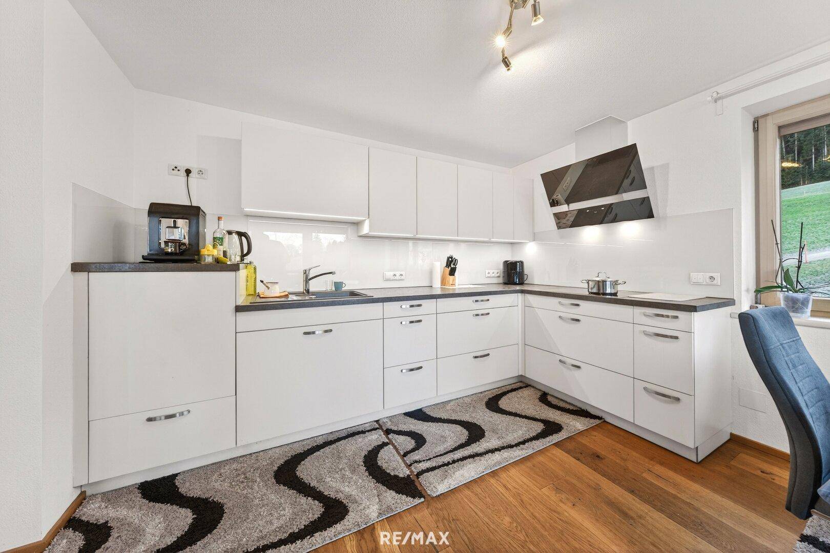 Moderne Küche mit weißen Hochglanzschränken, dunkler Arbeitsplatte und Holzboden.