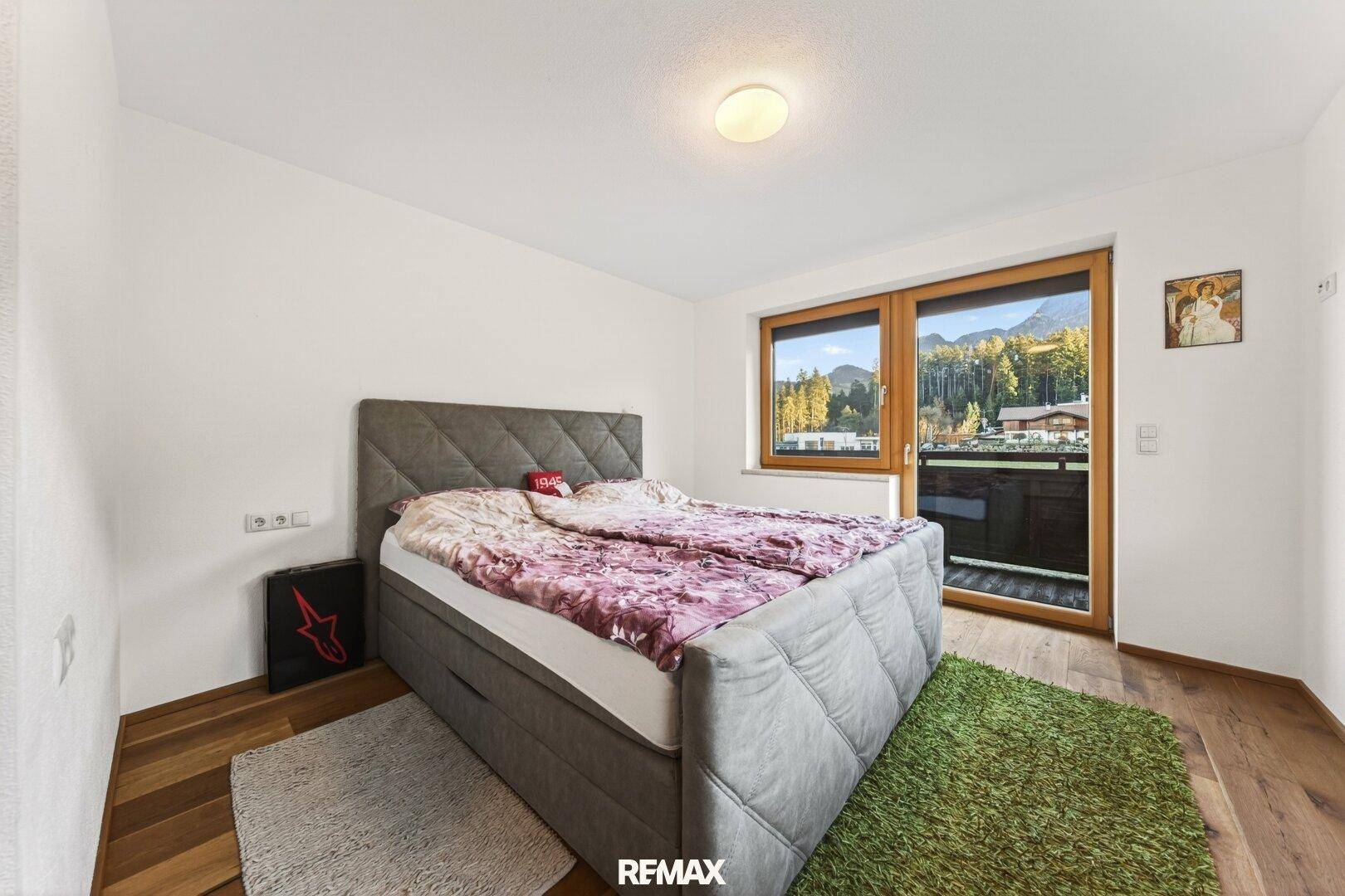 Helles Schlafzimmer mit modernem Bett, grünem Teppich und Balkonzugang mit Blick ins Grüne.