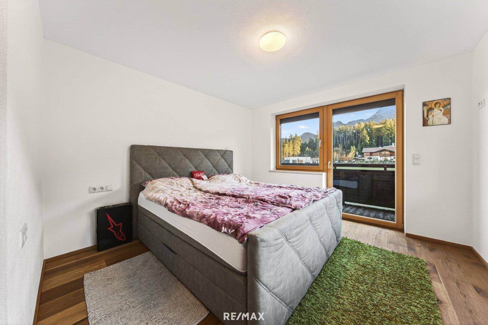Helles Schlafzimmer mit Doppelbett, Holzboden und Zugang zu einem Balkon mit Bergblick.