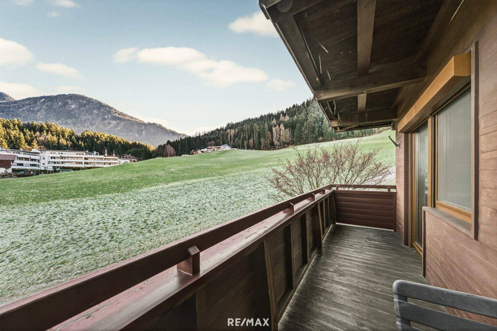 Geräumiger Holzbalkon mit weitem Blick auf die grüne Landschaft und die umliegenden Berge.