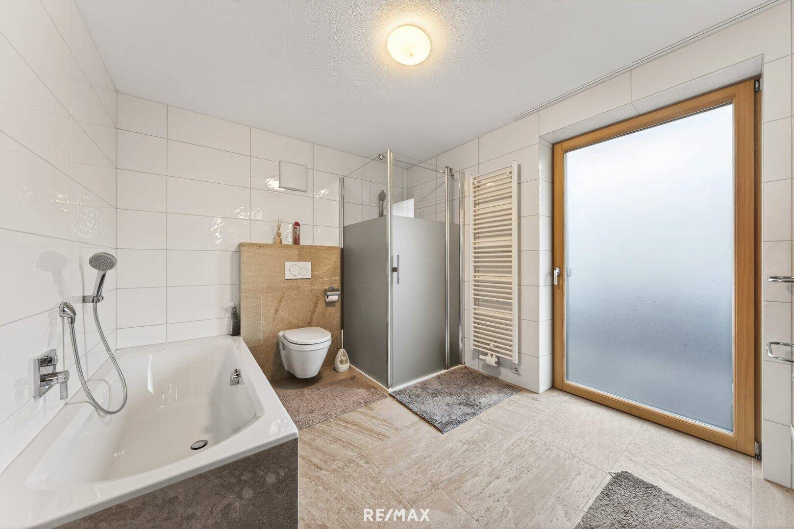 Modernes Badezimmer mit Badewanne, Dusche, WC und großem Fenster für Tageslicht.