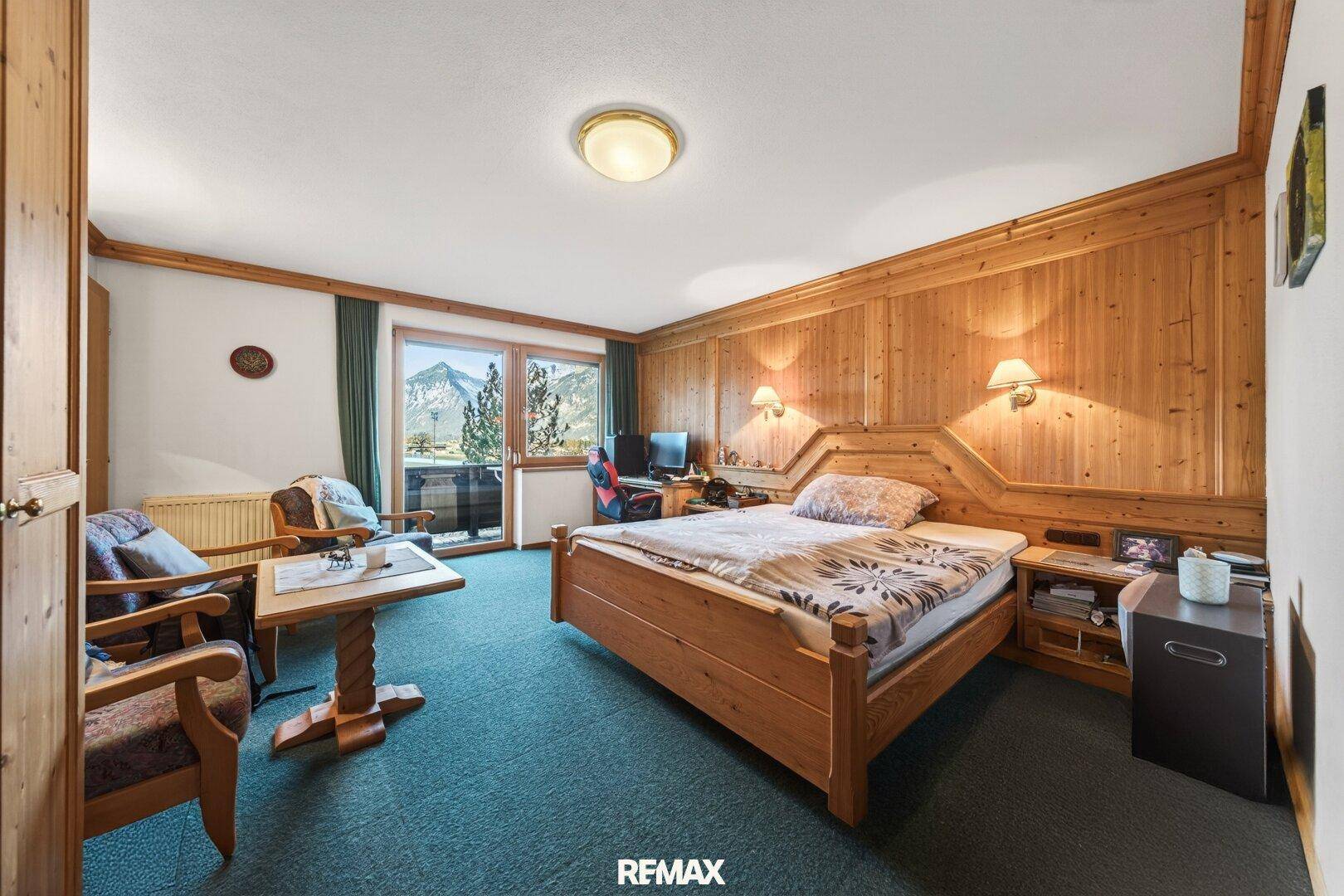 Traditionelles Schlafzimmer mit Holzvertäfelung, Doppelbett und Balkonzugang mit Bergblick.