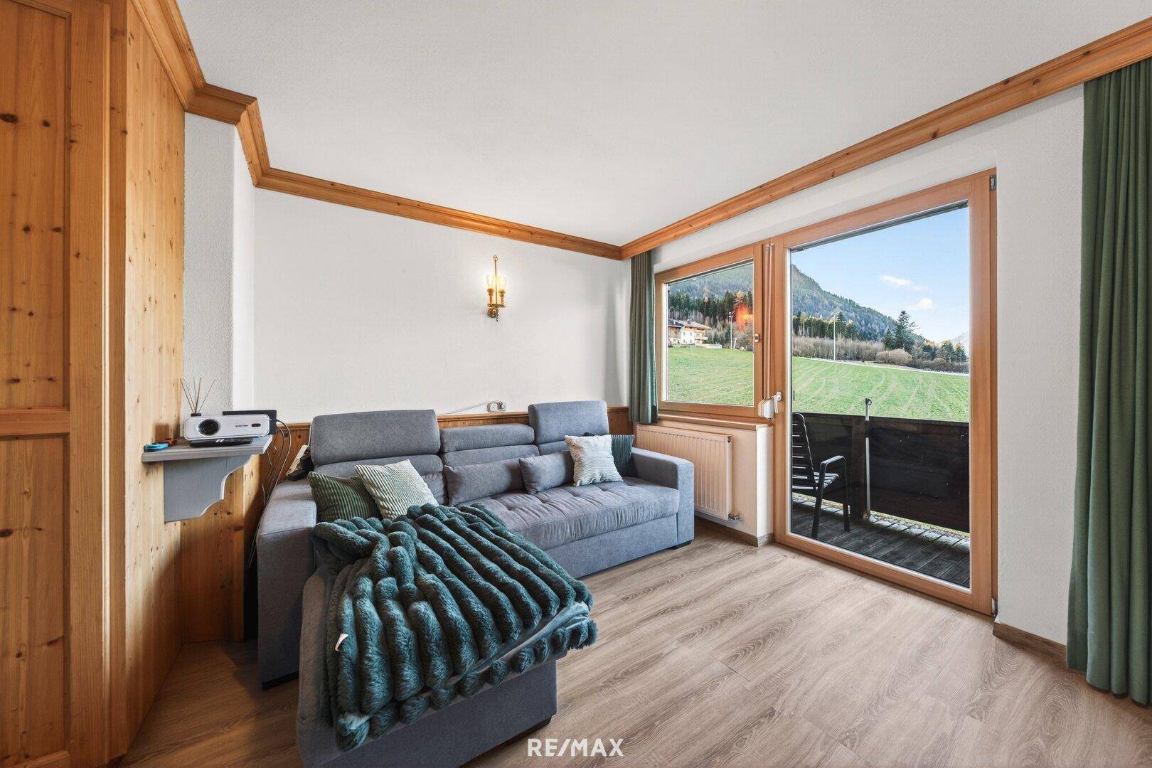 Helles Wohnzimmer mit Holzboden, Sofa und Zugang zu einem Balkon mit Landschaftsblick.