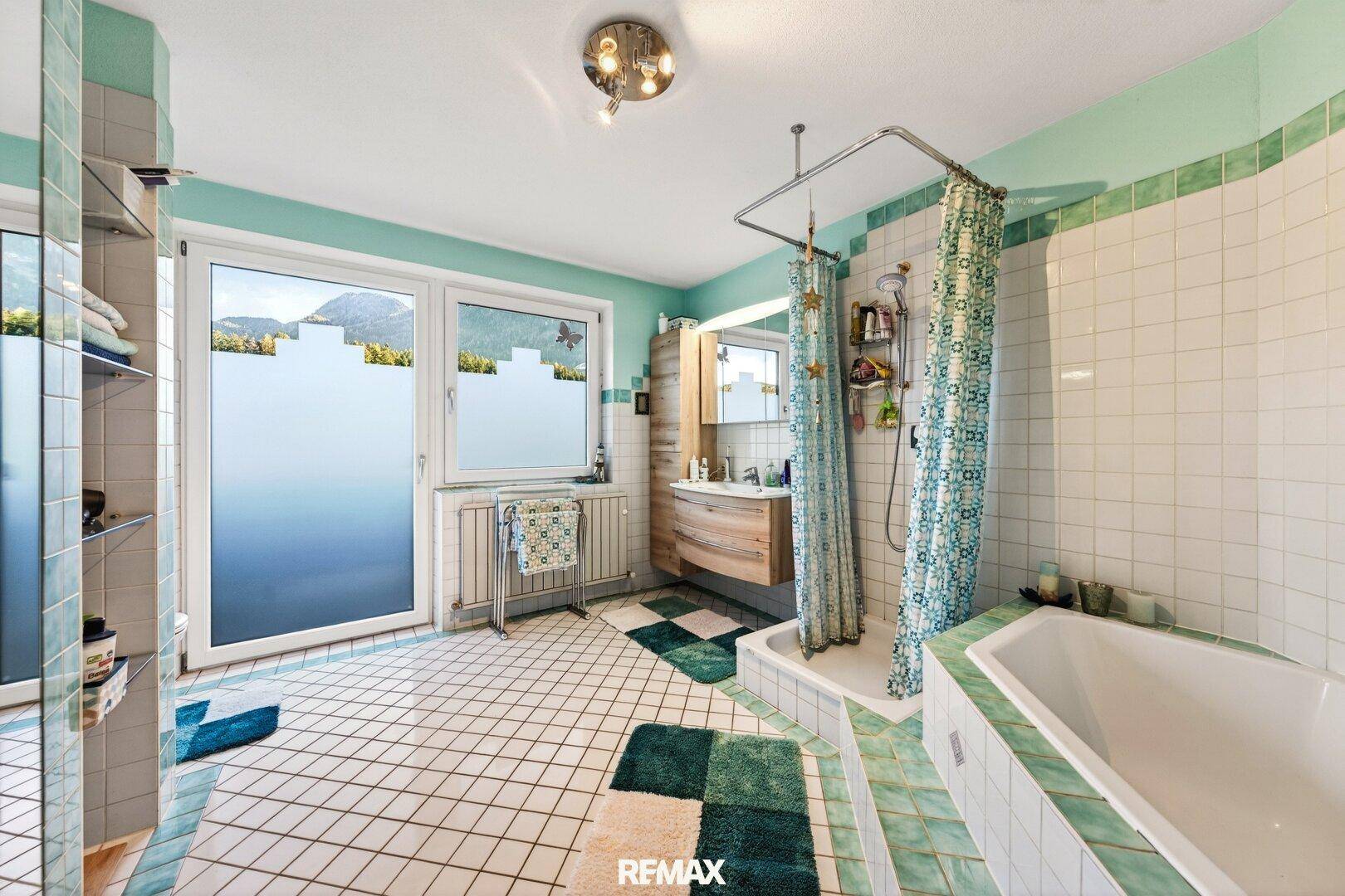 Geräumiges Badezimmer mit grünen und weißen Fliesen, Badewanne, Dusche und Fenster.