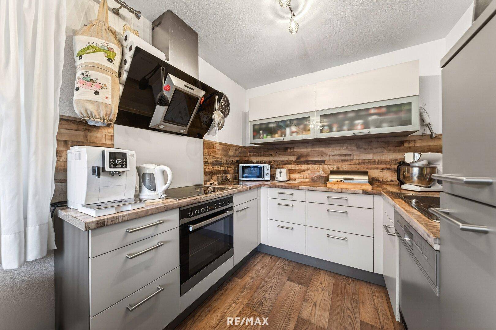 Moderne Küche mit grauen und weißen Schränken, Holzakzenten und integrierten Geräten.