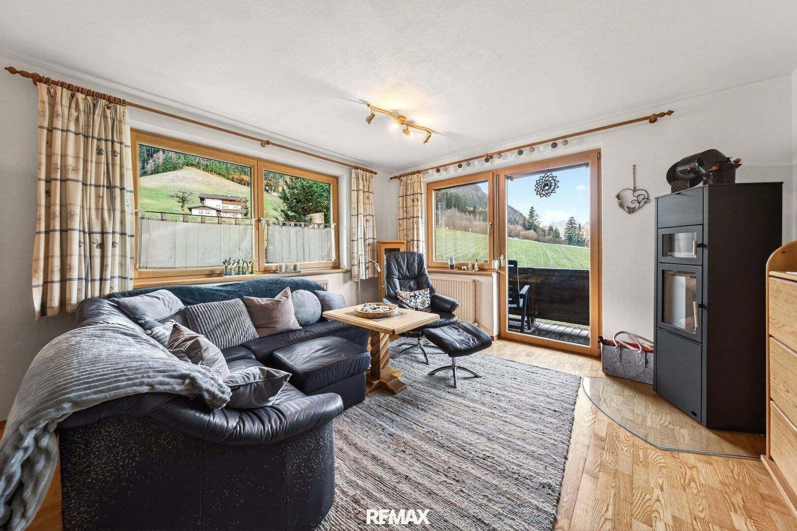 Gemütliches Wohnzimmer mit Ledersofa, Kaminofen und Zugang zu einem Balkon mit Bergblick.