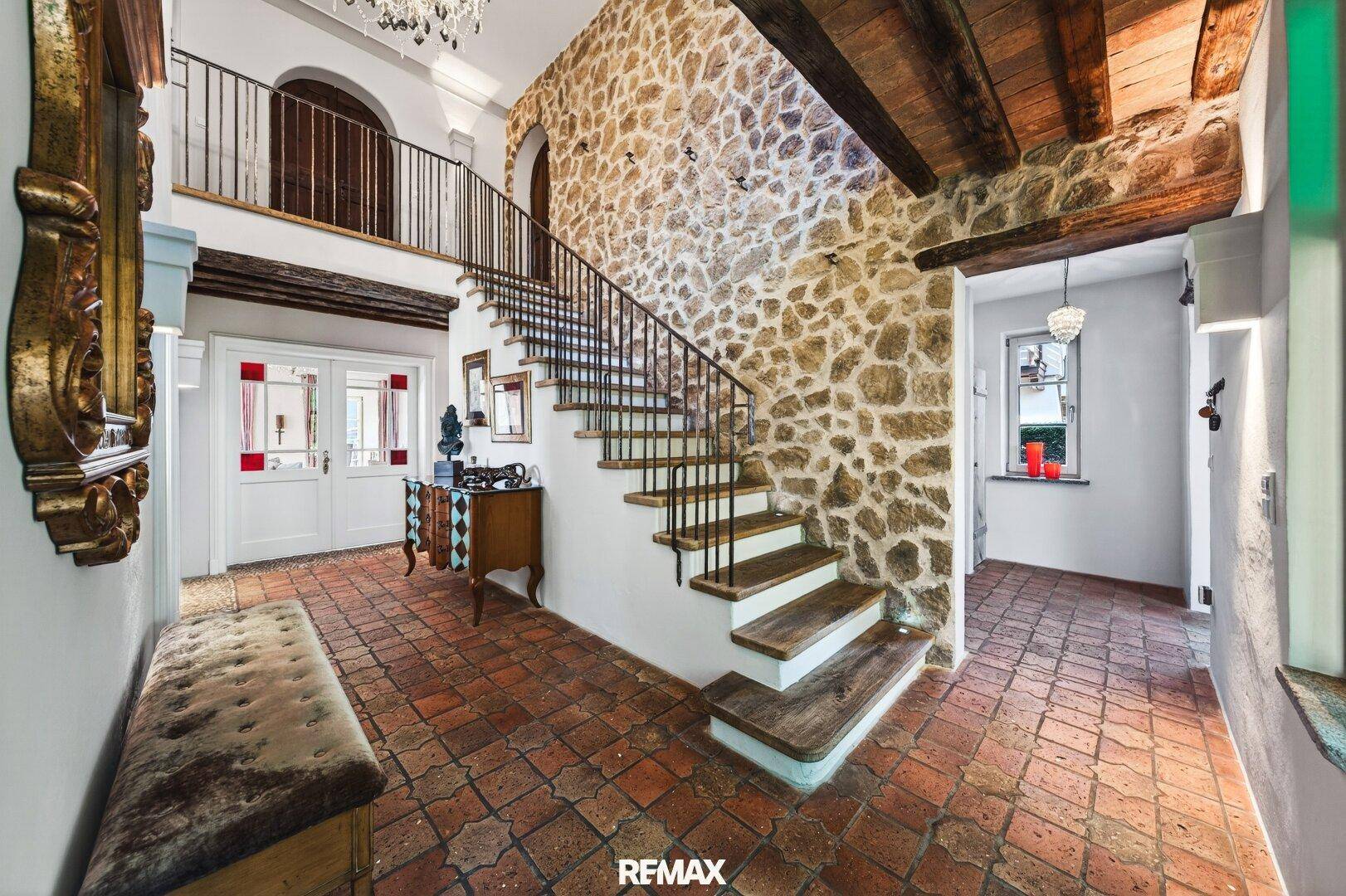 Beeindruckender Eingangsbereich mit Steinfliesen, freiliegenden Holzbalken und einer eleganten Treppe.