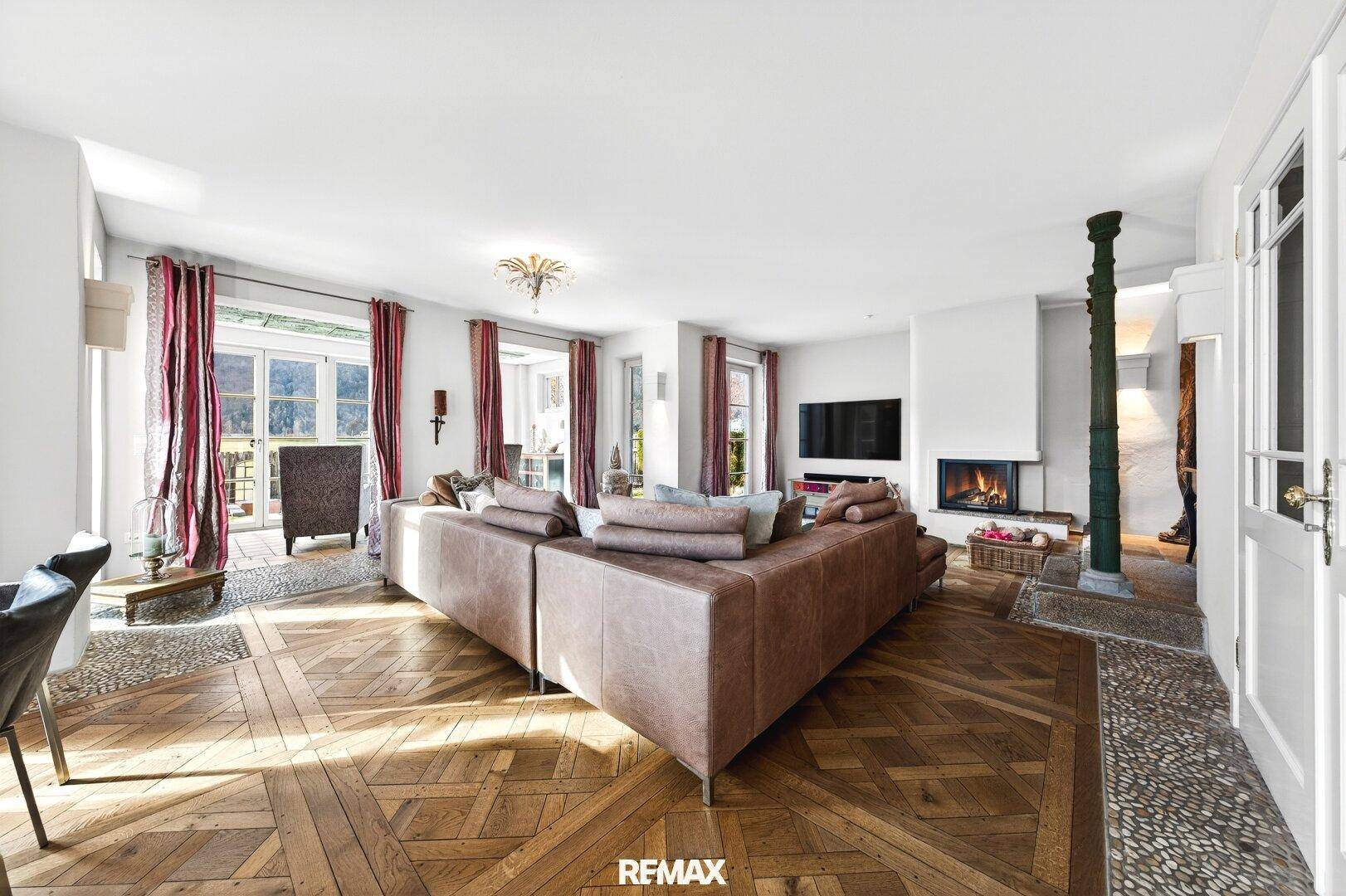 Gemütliches Wohnzimmer mit großem Sofa, Kamin und gemustertem Parkettboden.