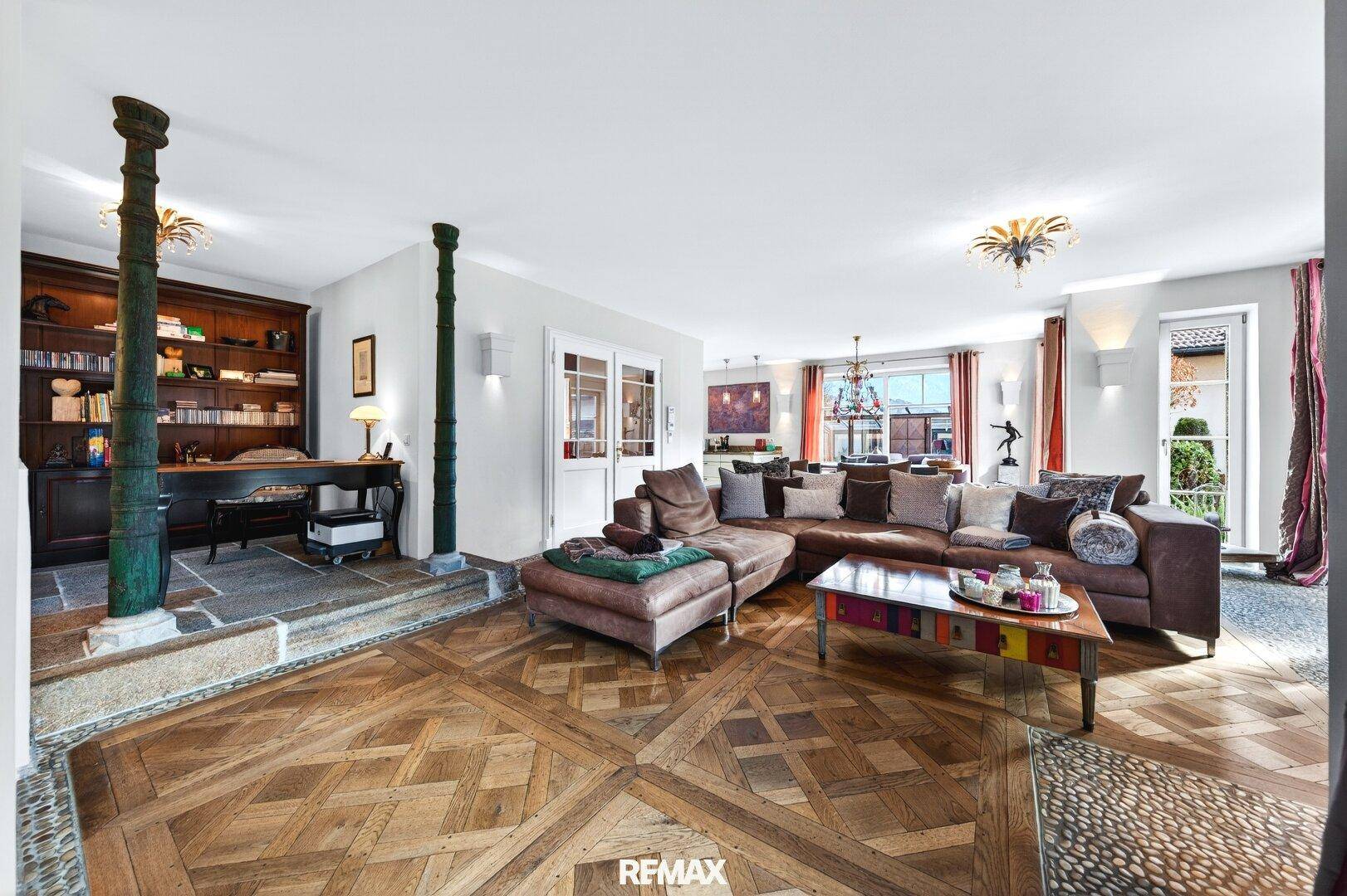 Geräumiges Wohnzimmer mit gemustertem Parkettboden, gemütlicher Sitzecke und integriertem Arbeitsbereich.