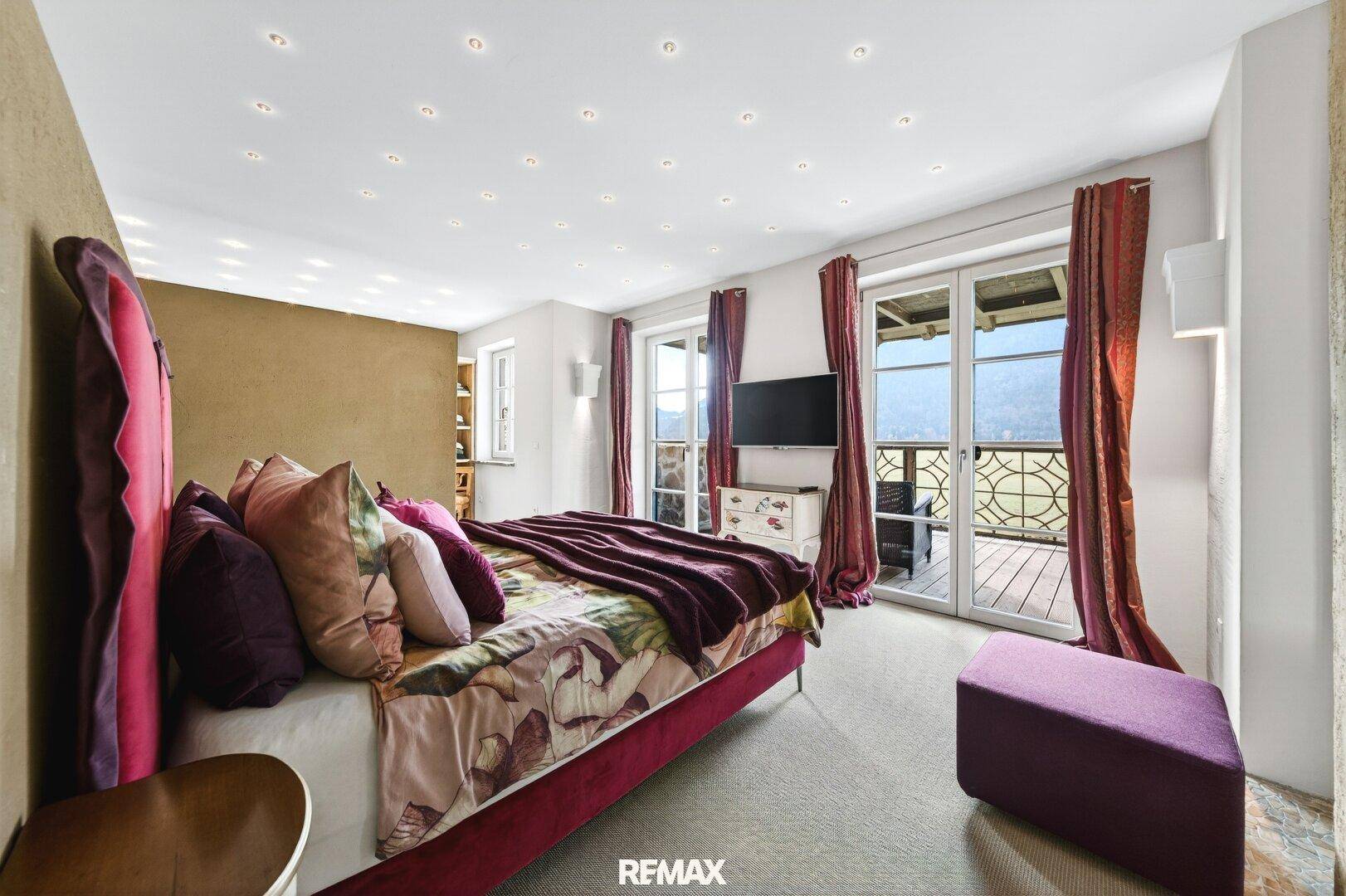 Helles Schlafzimmer mit Zugang zum Balkon, Teppichboden und einem großen Bett mit farbigen Kissen.