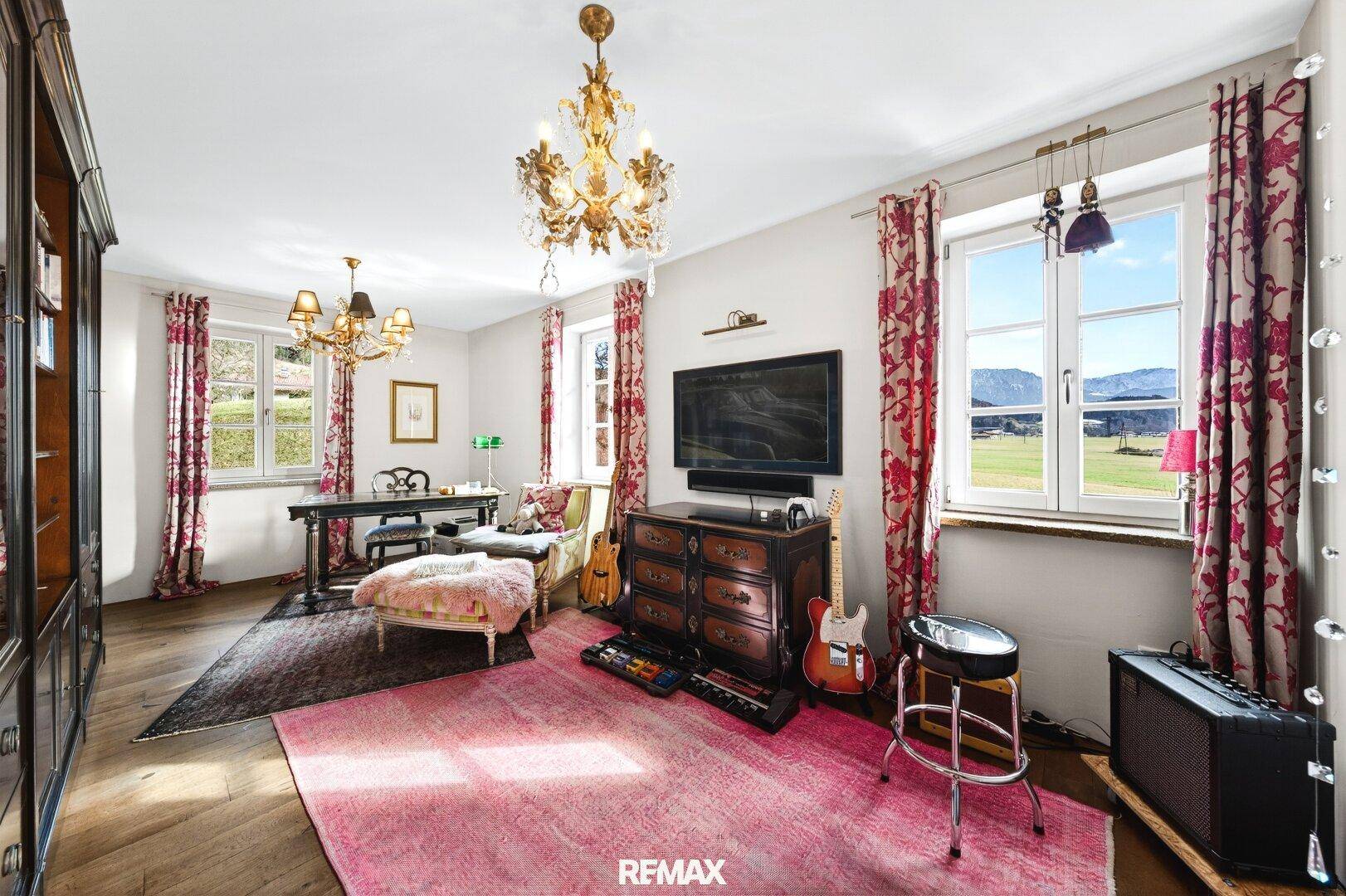 Stilvolles Wohnzimmer mit Kronleuchtern, Holzboden und Blick auf die umliegende Landschaft.