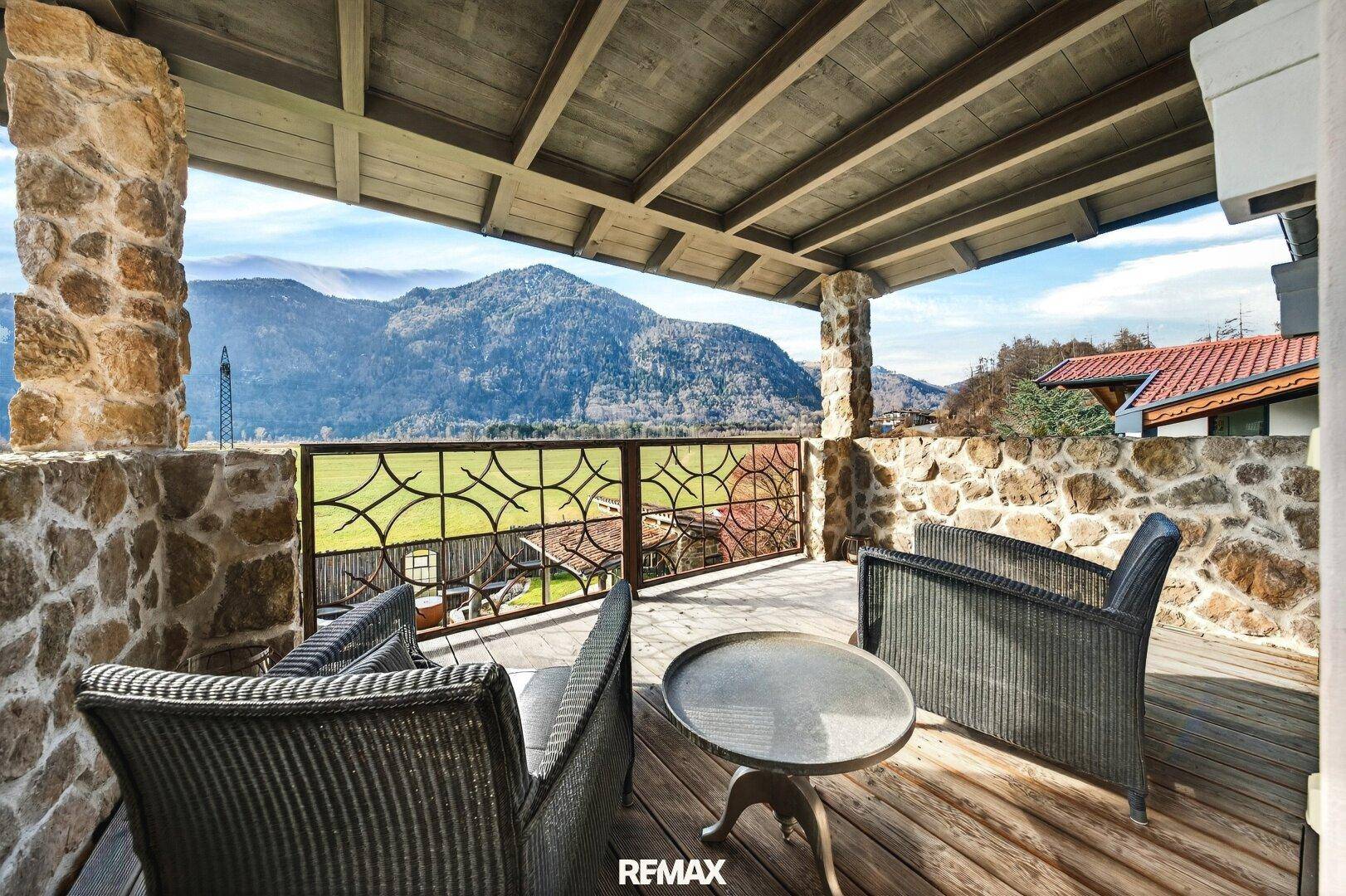 Überdachter Balkon mit Sitzgelegenheiten, Steinpfeilern und weitem Bergblick.