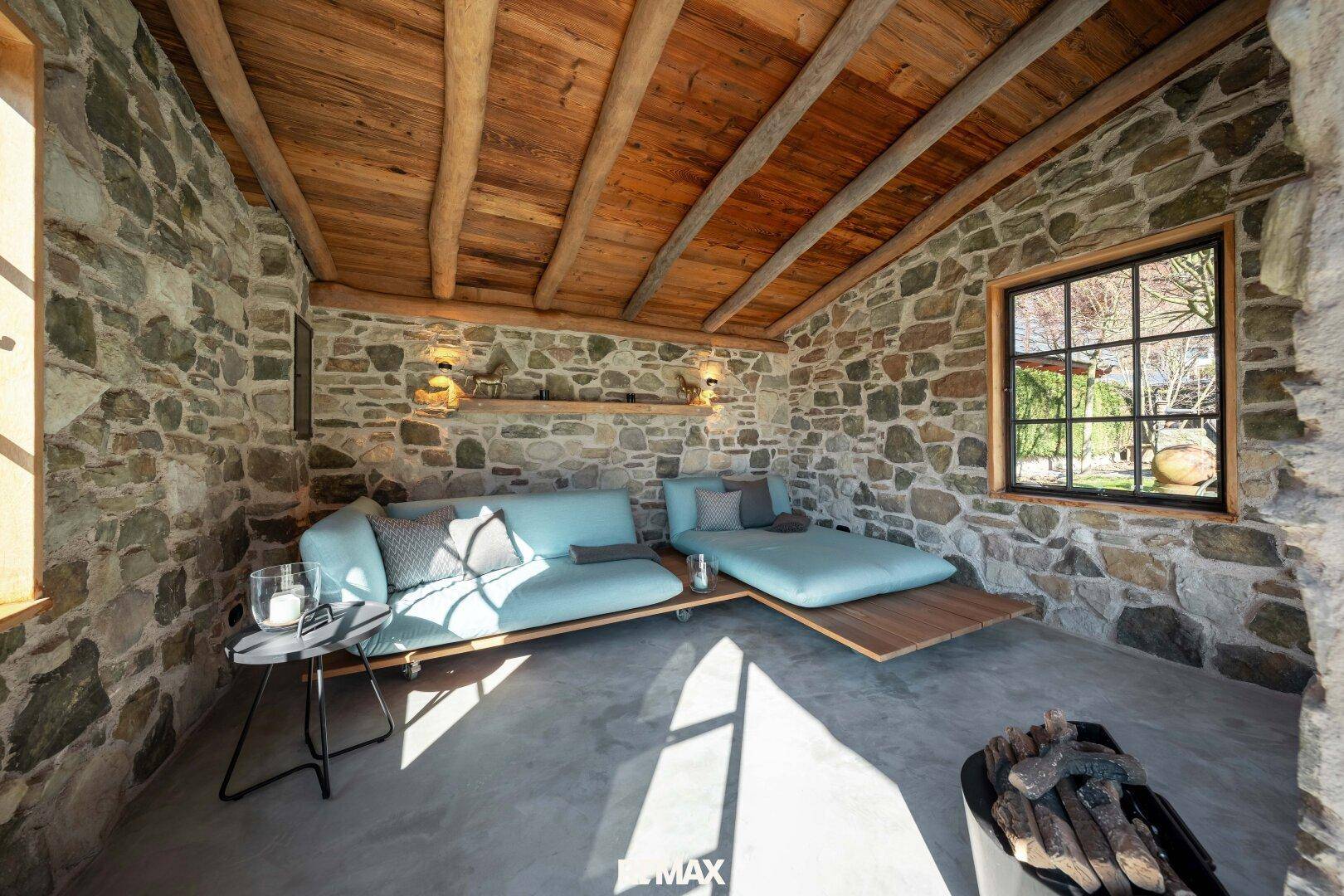 Gemütlicher Lounge-Bereich mit Steinwänden, Holzbalkendecke und bequemen Sitzgelegenheiten.