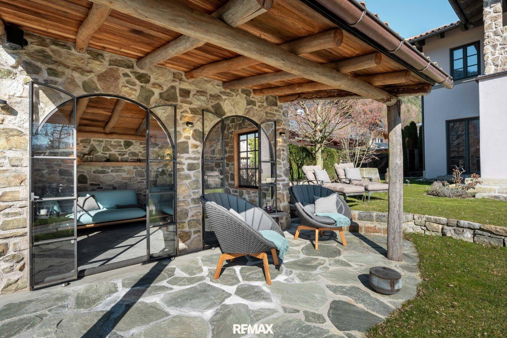 Steinpflasterter Terrassenbereich vor dem Gartenhaus mit bequemen Outdoor-Sesseln.