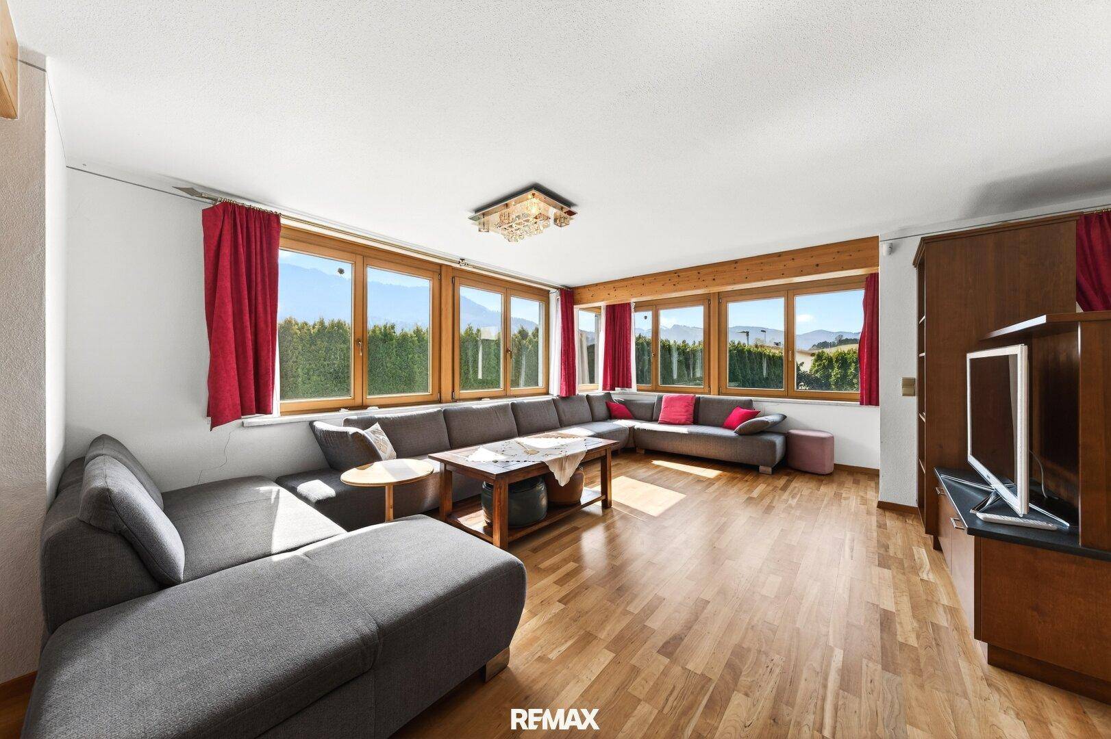 Helles Wohnzimmer mit großem Ecksofa, Holzboden und weitem Ausblick durch die Fensterfront.